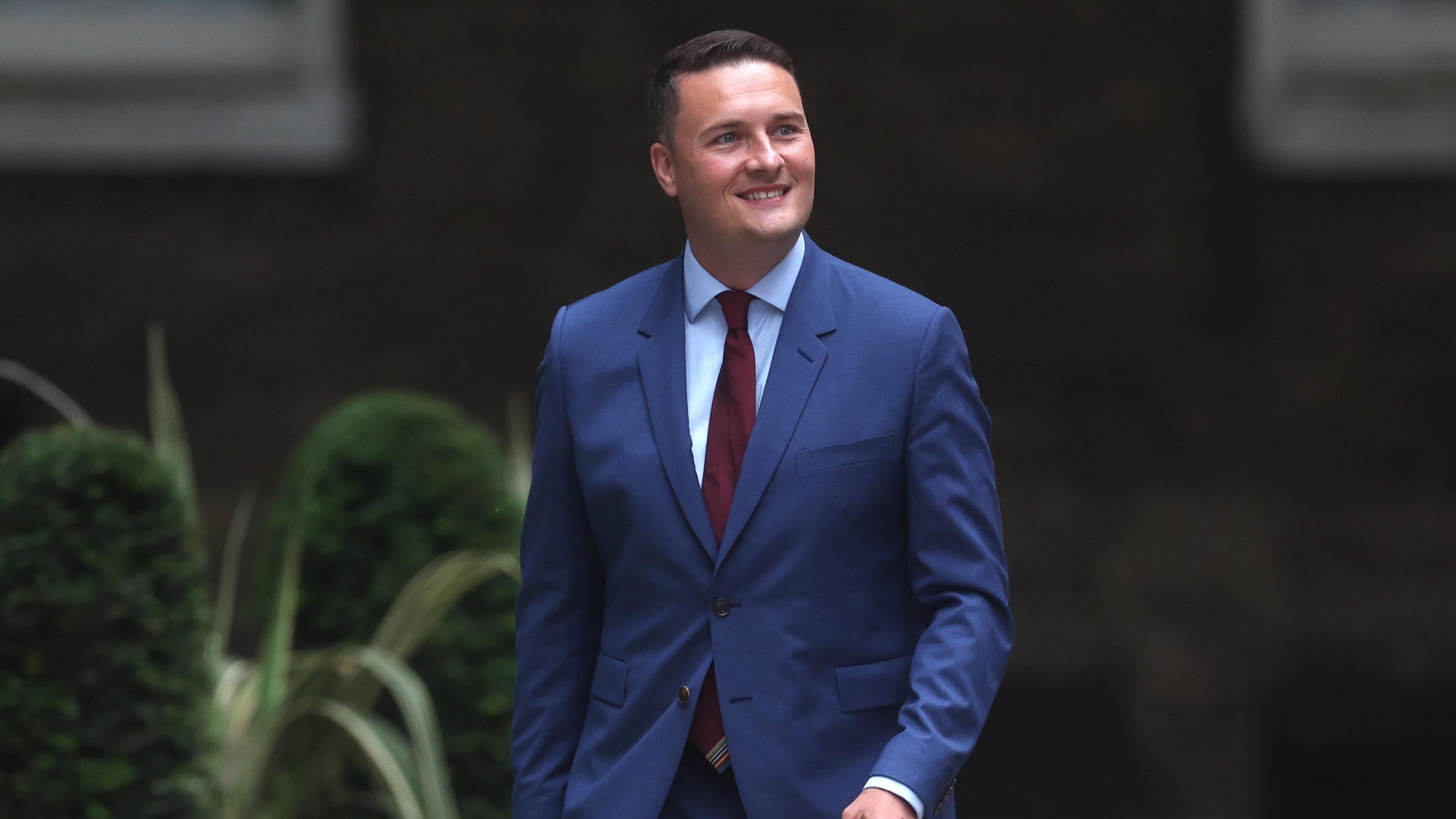 Wes Streeting smiling as he walks down a street.