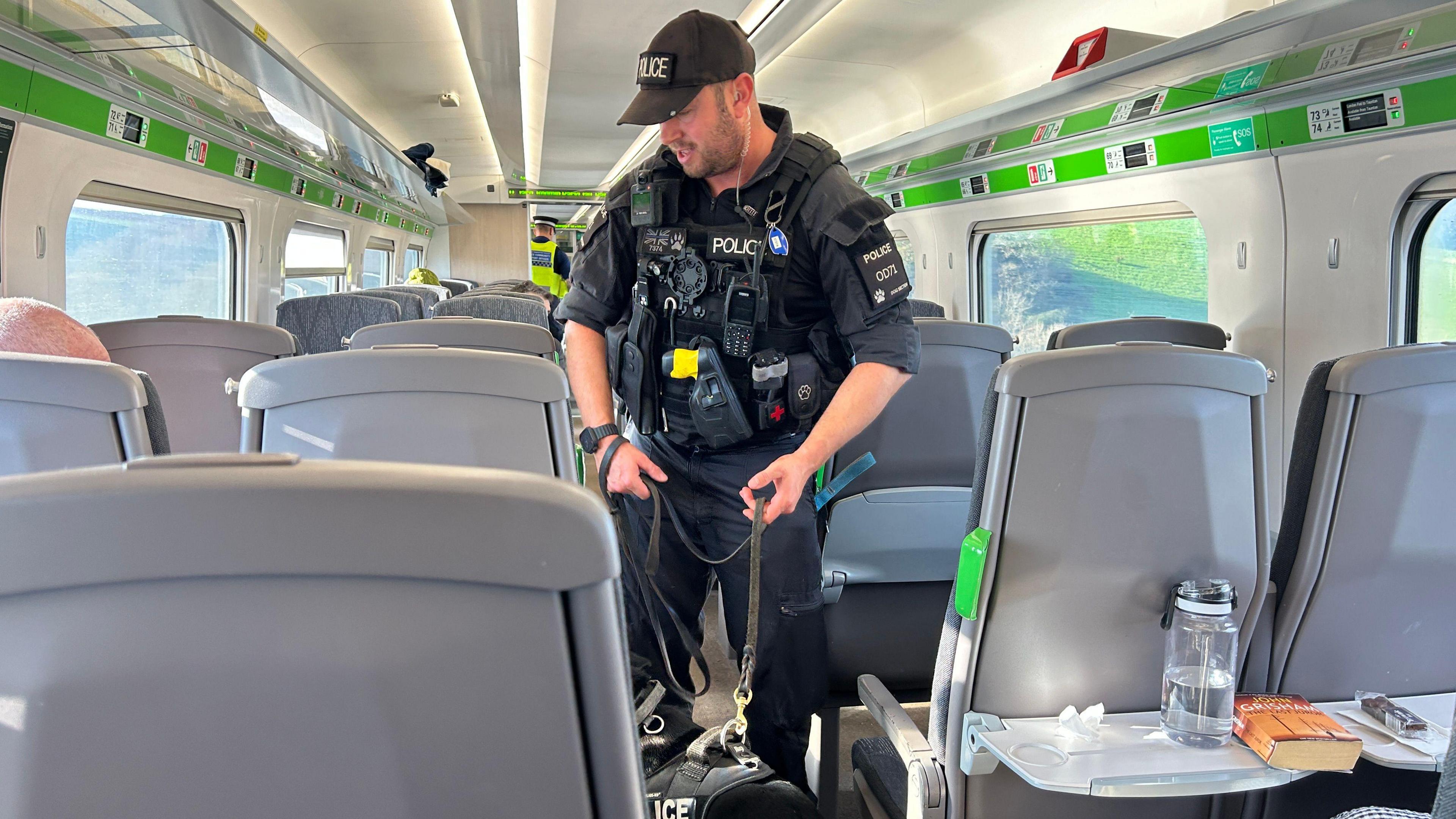 A police officer and a black sniffer dog on a train checking passengers fro drugs