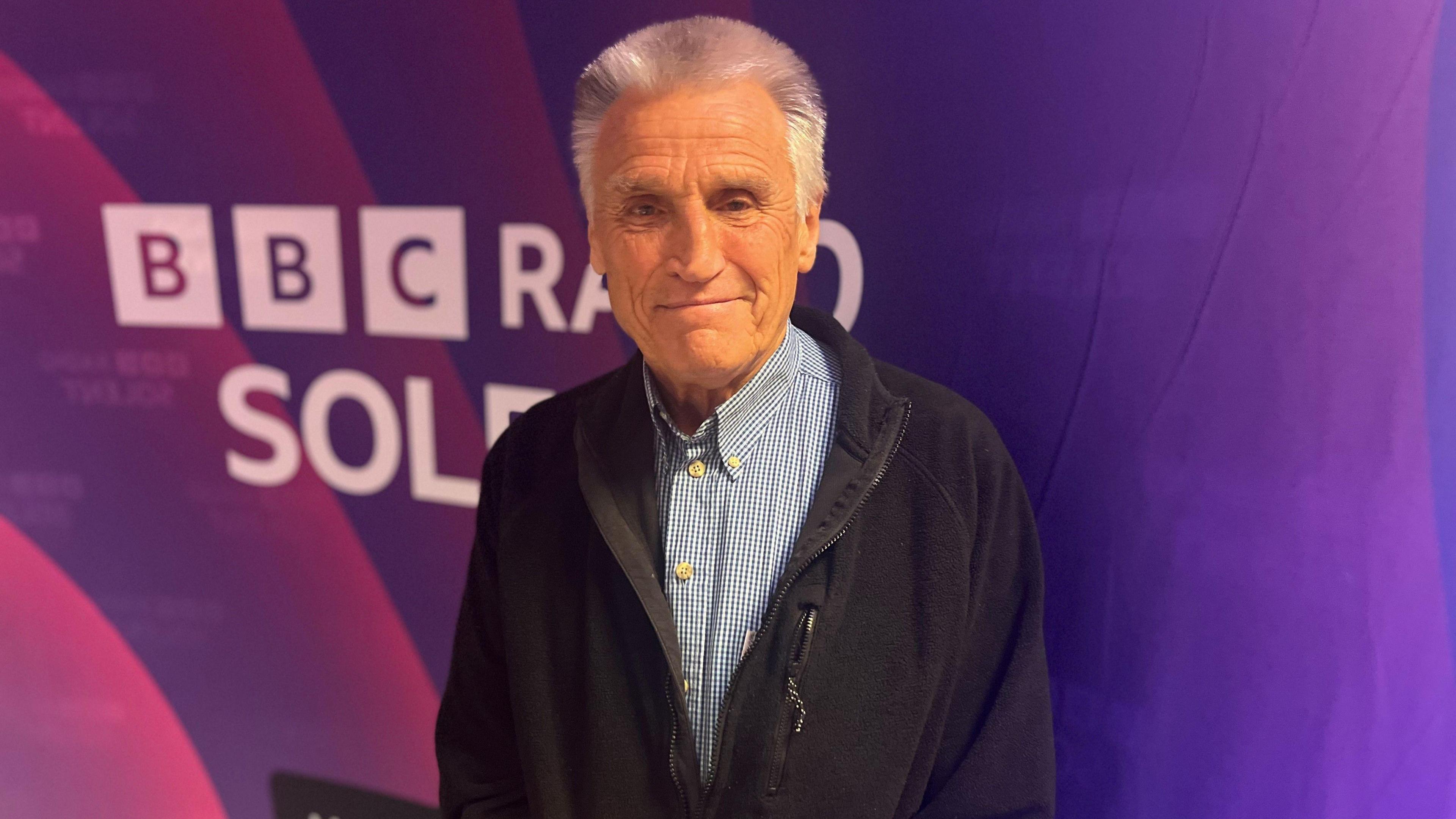 Bob Lakin a grey haired man stood in front of a purple BBC Radio Solent backdrop