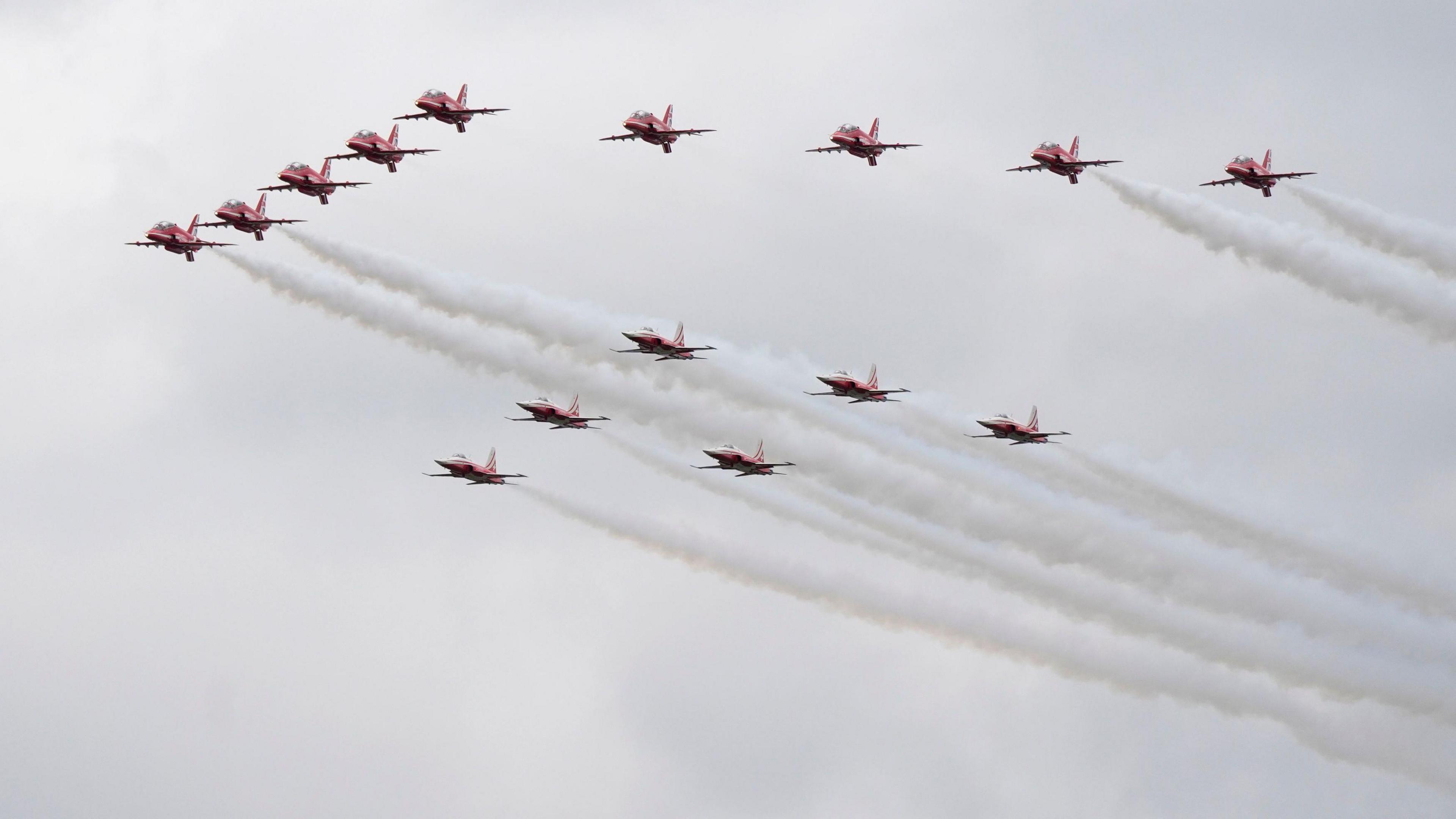 Aircraft are seen in the sky during a flight display. The aircraft are red, with white condensation trails.