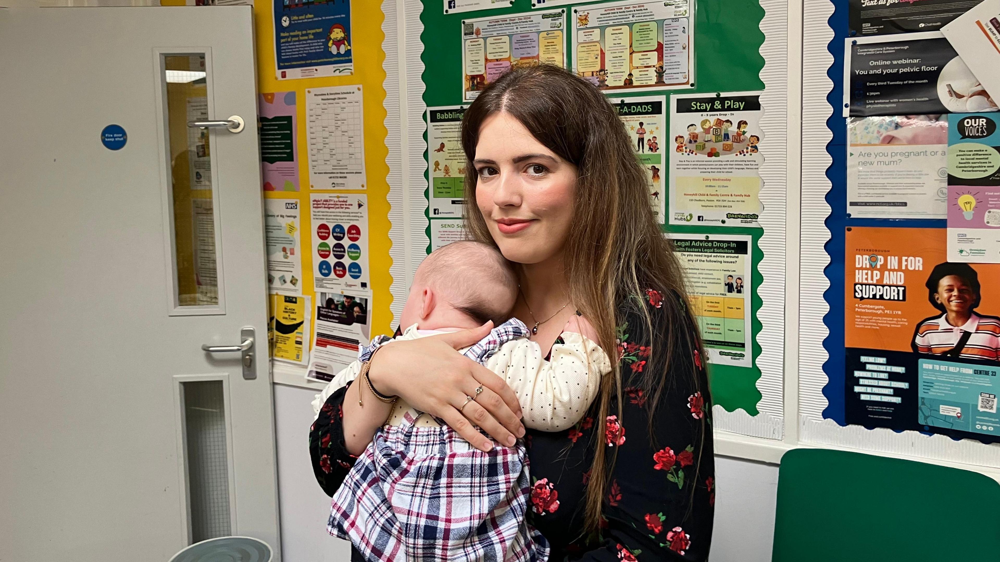 Jessica wearing a black and red top holding her baby girl- wearing a checked dress 