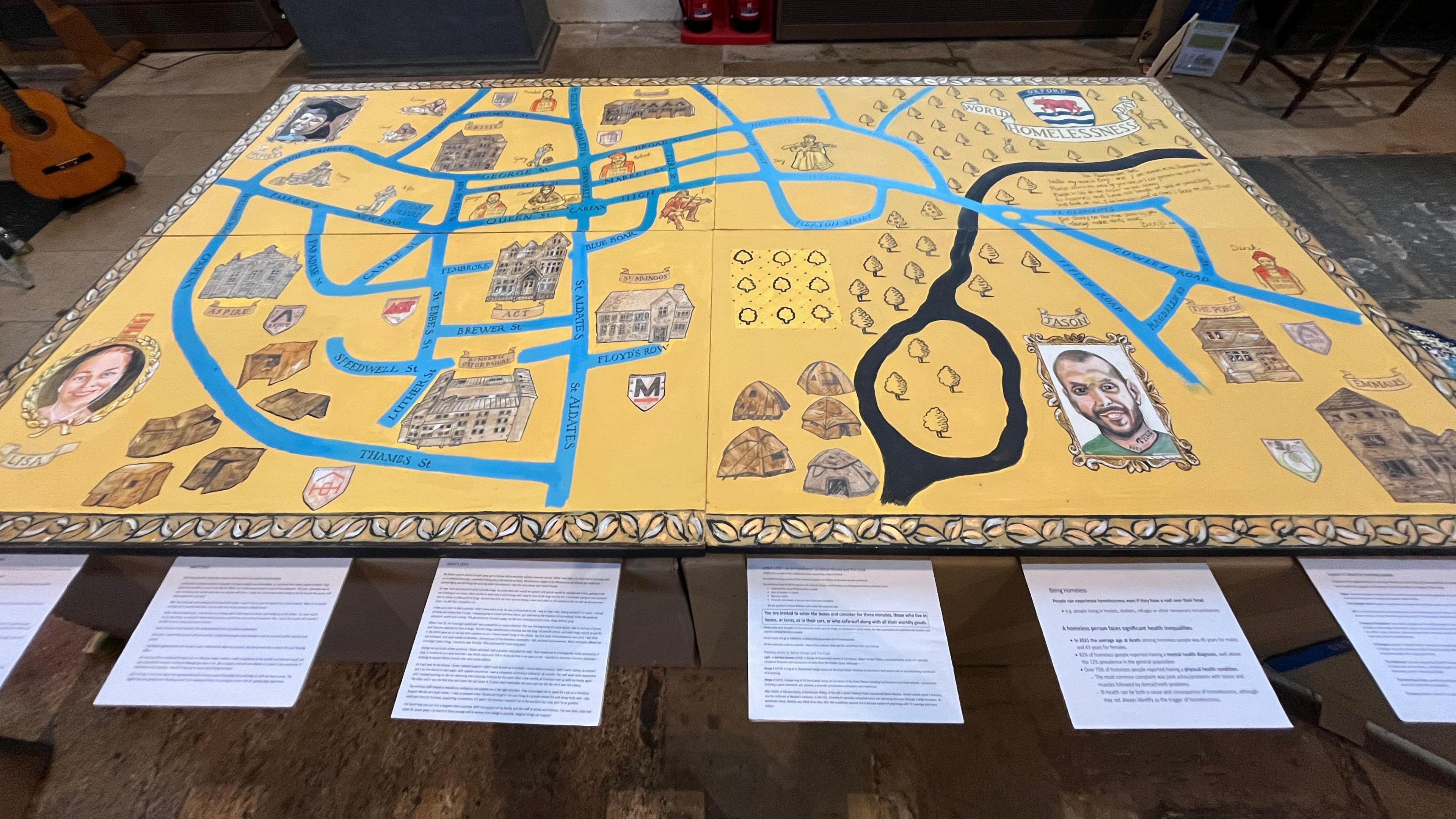 A Map of Oxford made with a yellow base and blue card coloured streets. There are also portraits of homeless people and their diaries, alongside painted buildings.