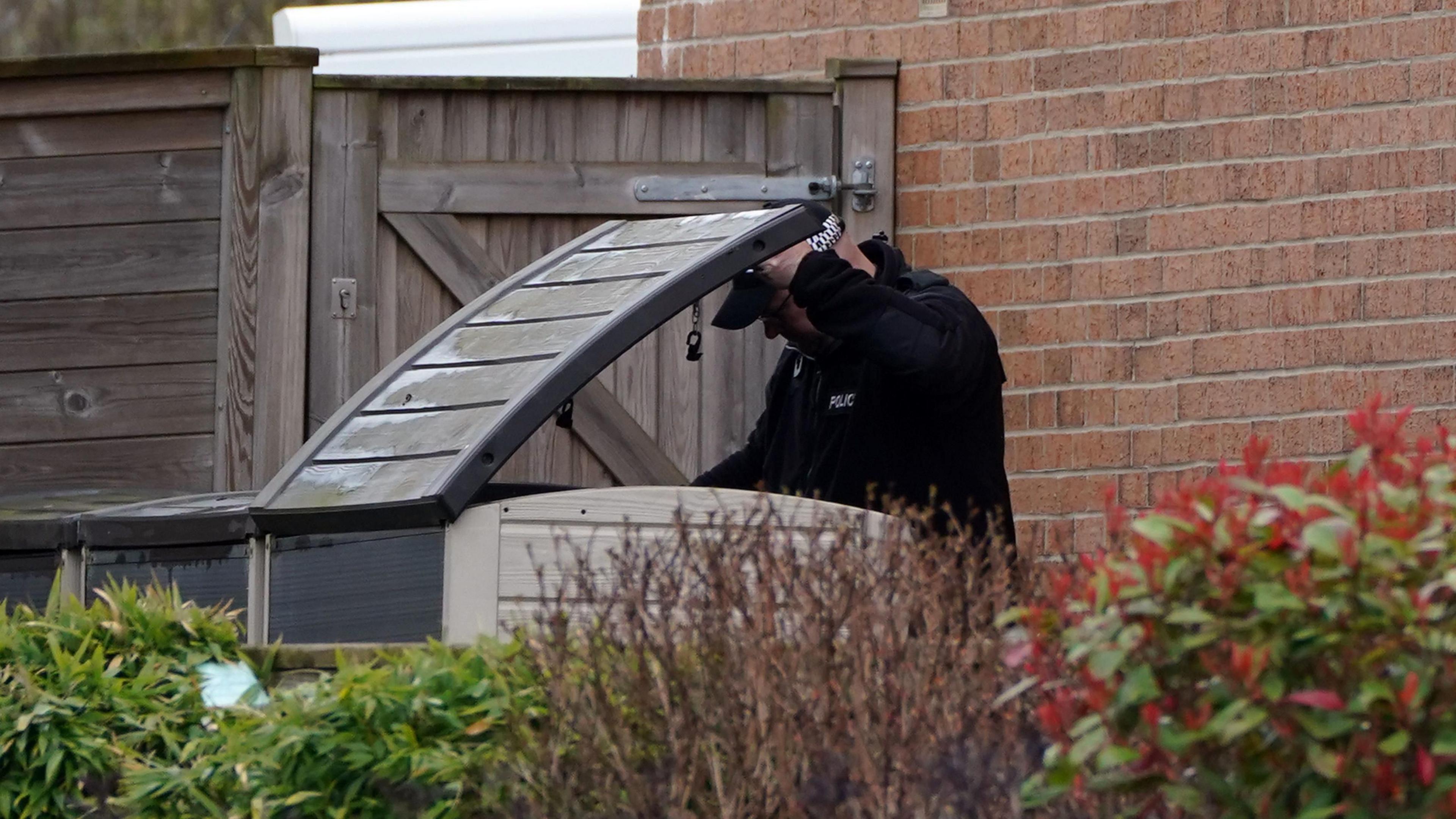 A police officer looking in a garden storage box. He is holding the lid open.