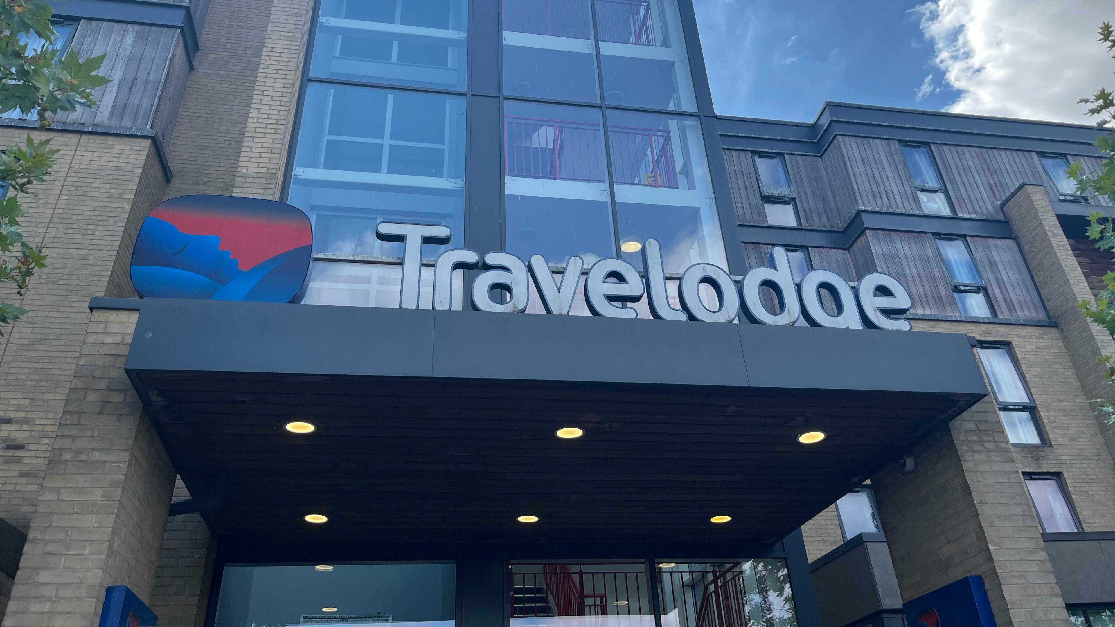 A Travelodge hotel on Newmarket Road in Cambridge. There is a Travelodge sign and logo on the entrance of the building.