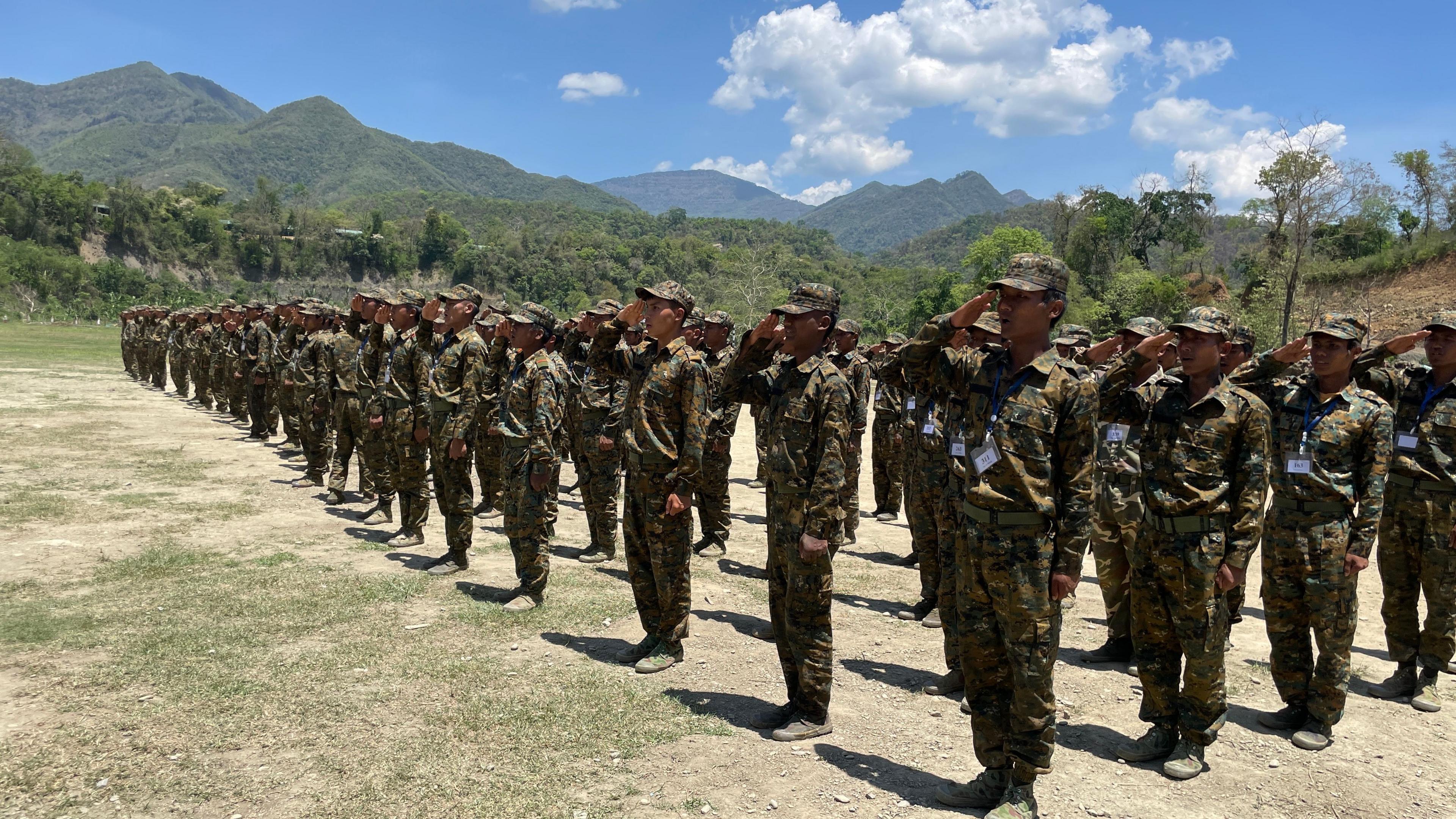 Recruits at a training ground for the rebel military, with forested hills in the background