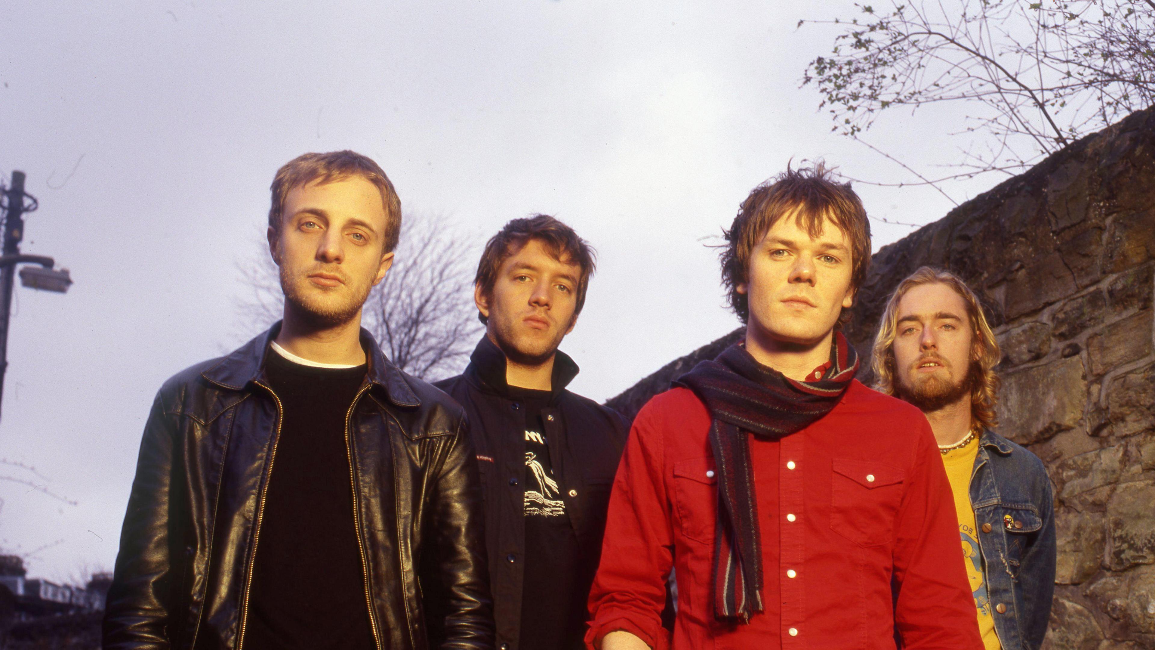 Four men standing outside and looking into the camera with serious expressions on their faces