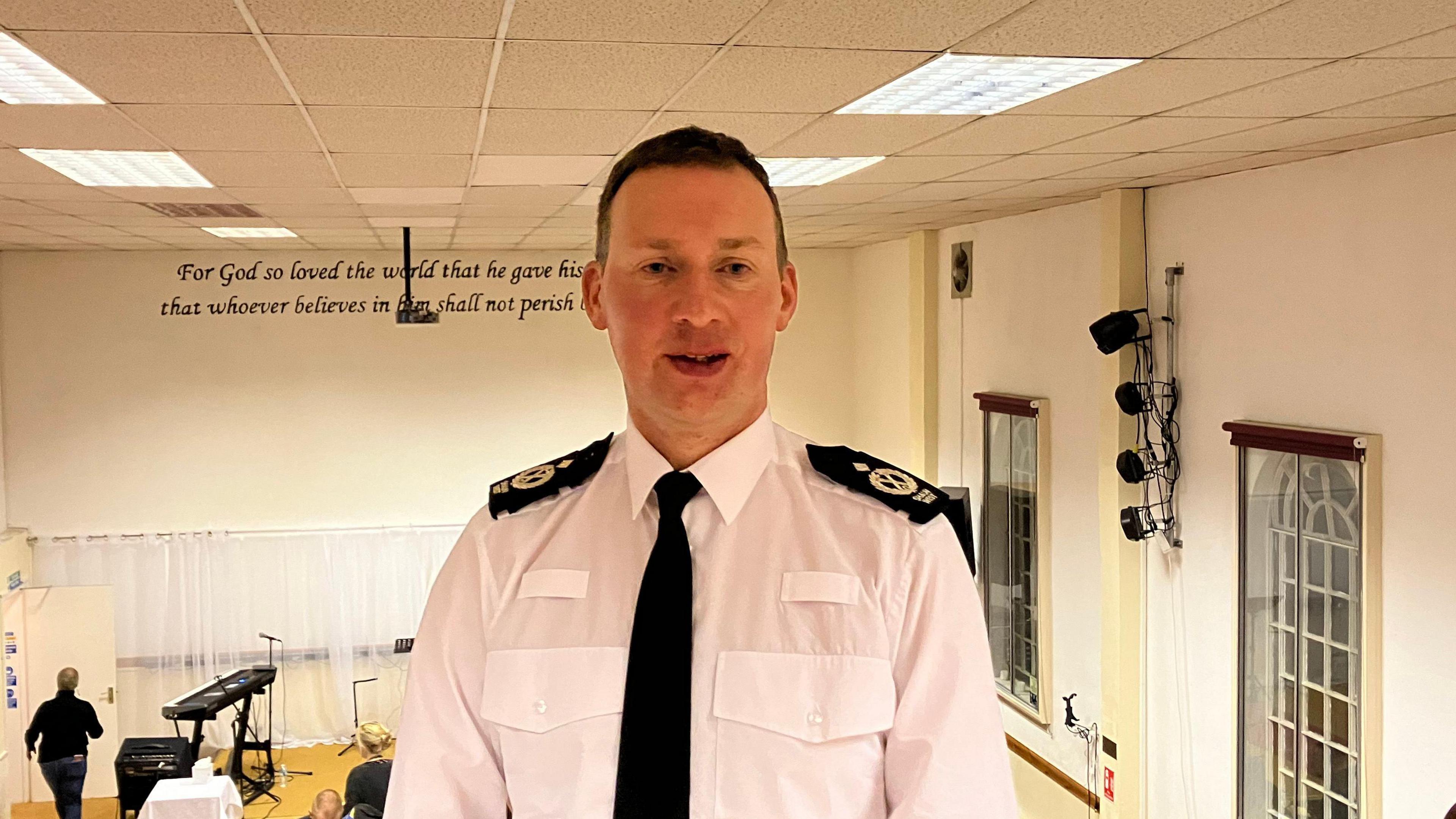 Det Ch Con Shaun West pictured in what appears to be a church. He is in uniform and wears a white shirt and a black tie. 