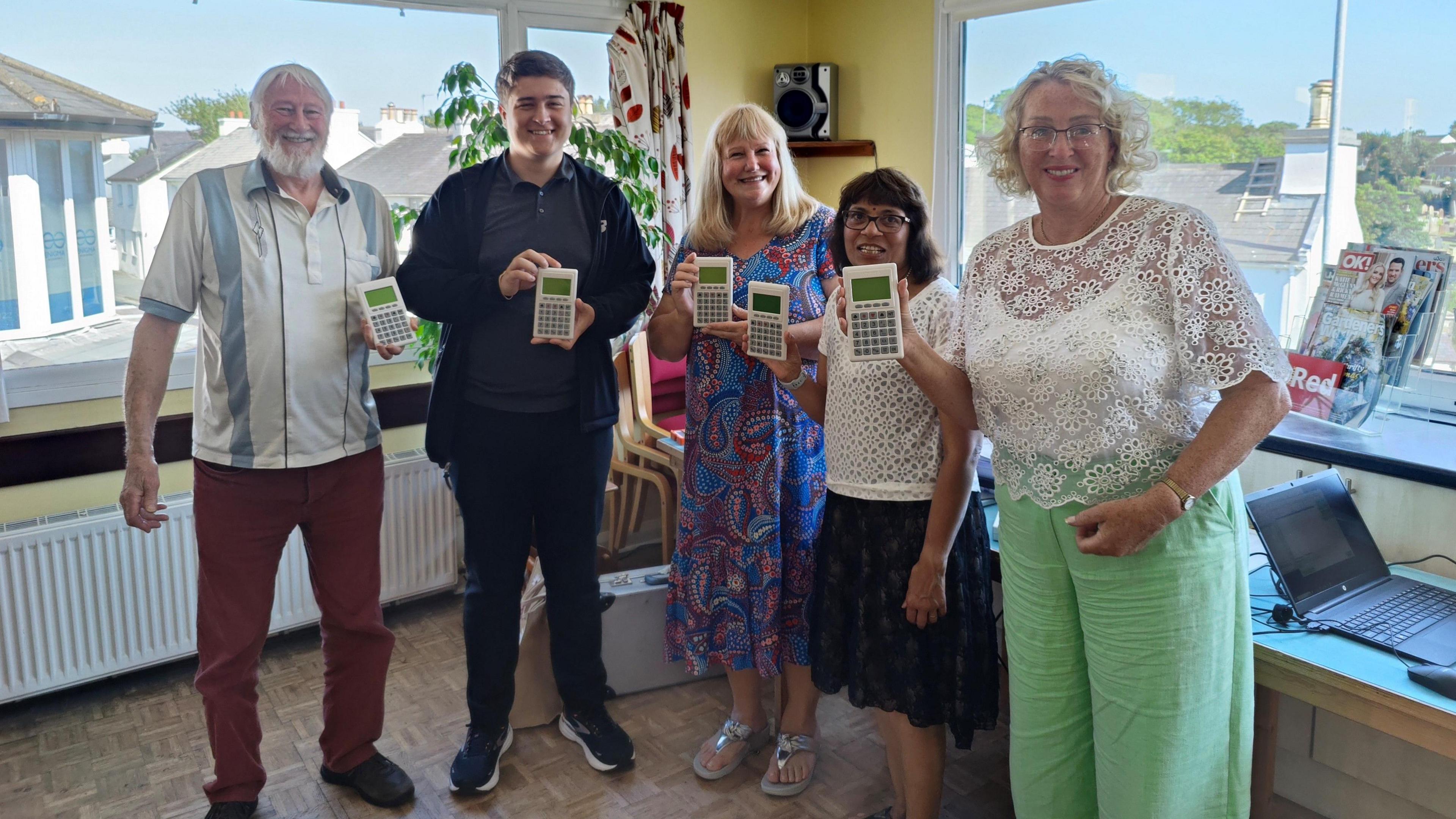 A group of two men and three women each holding what looks like calculators- the new machines for scoring- and smiling.