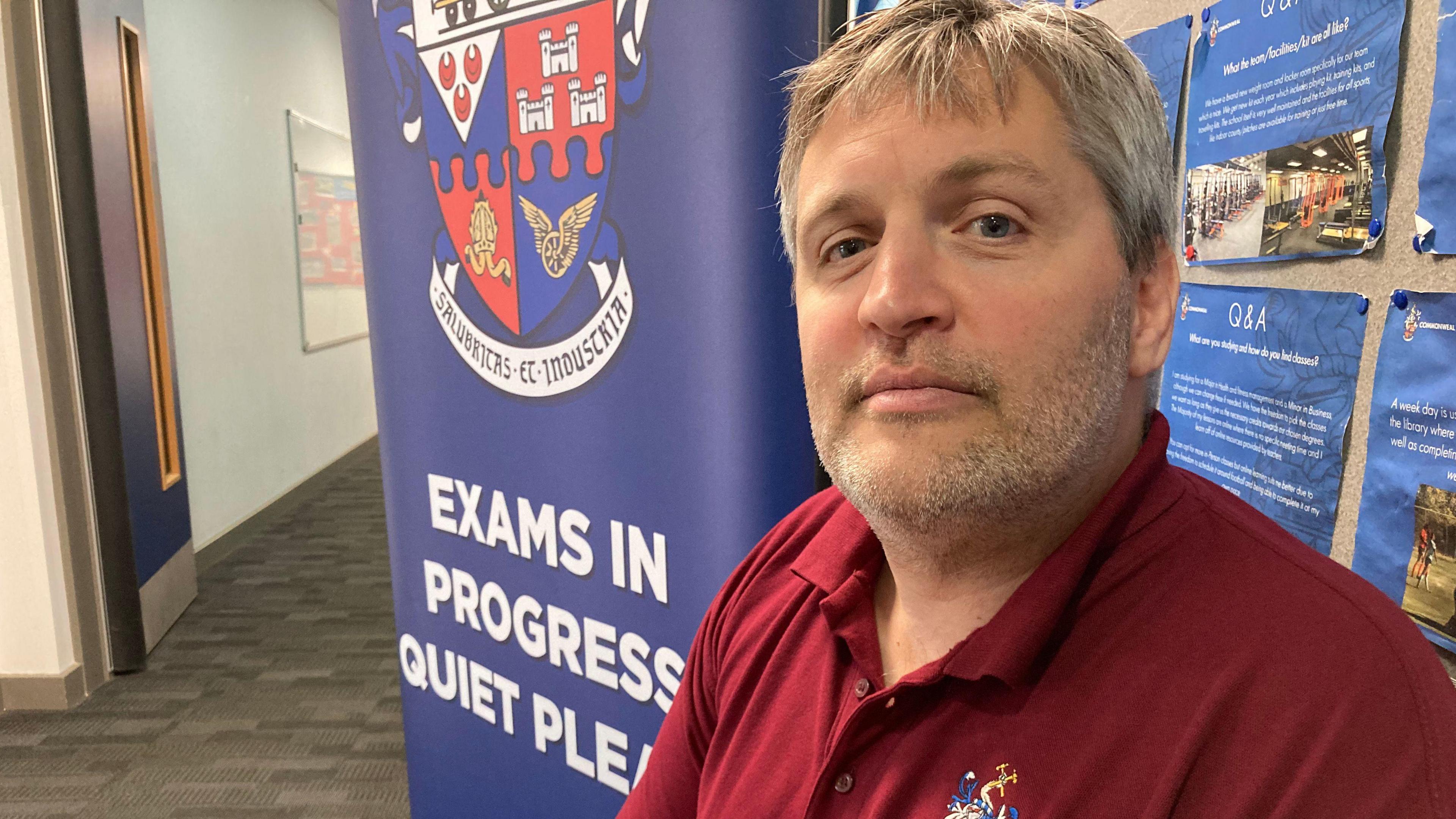 Headteacher Charles Drew sat in front of a sign that says 'Exams in progress. Quiet Please.'