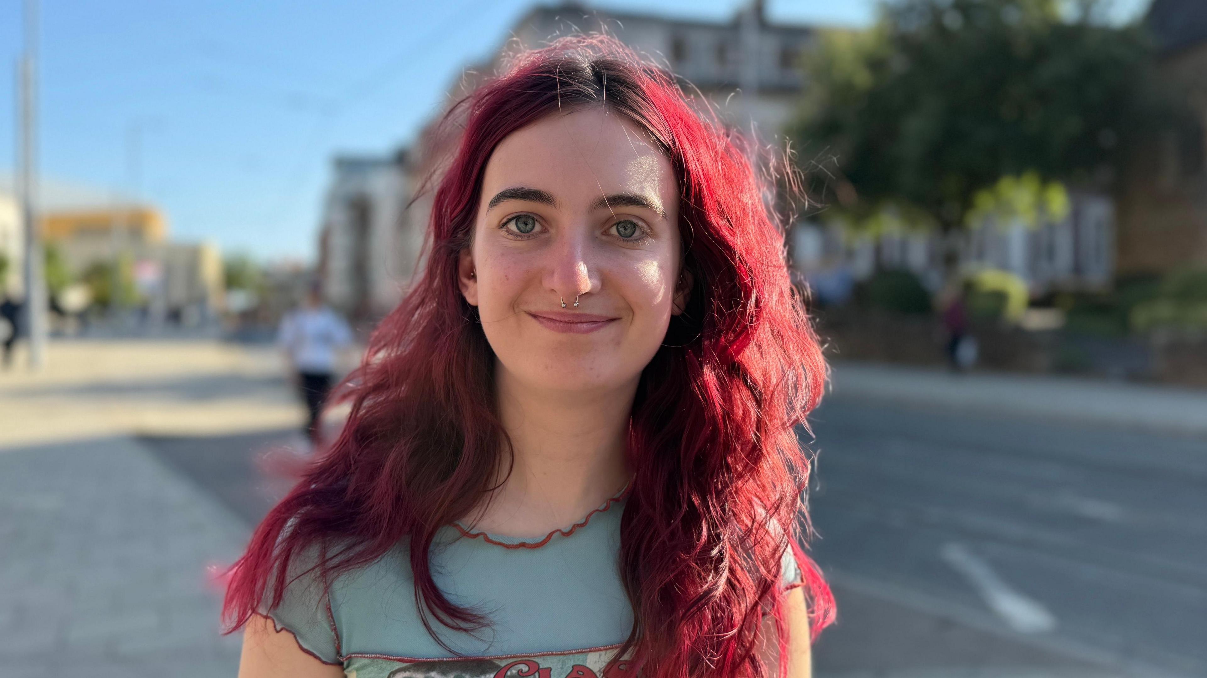 Female student with dyed red hair and a blue short sleeved top stood in Nottingham city centre