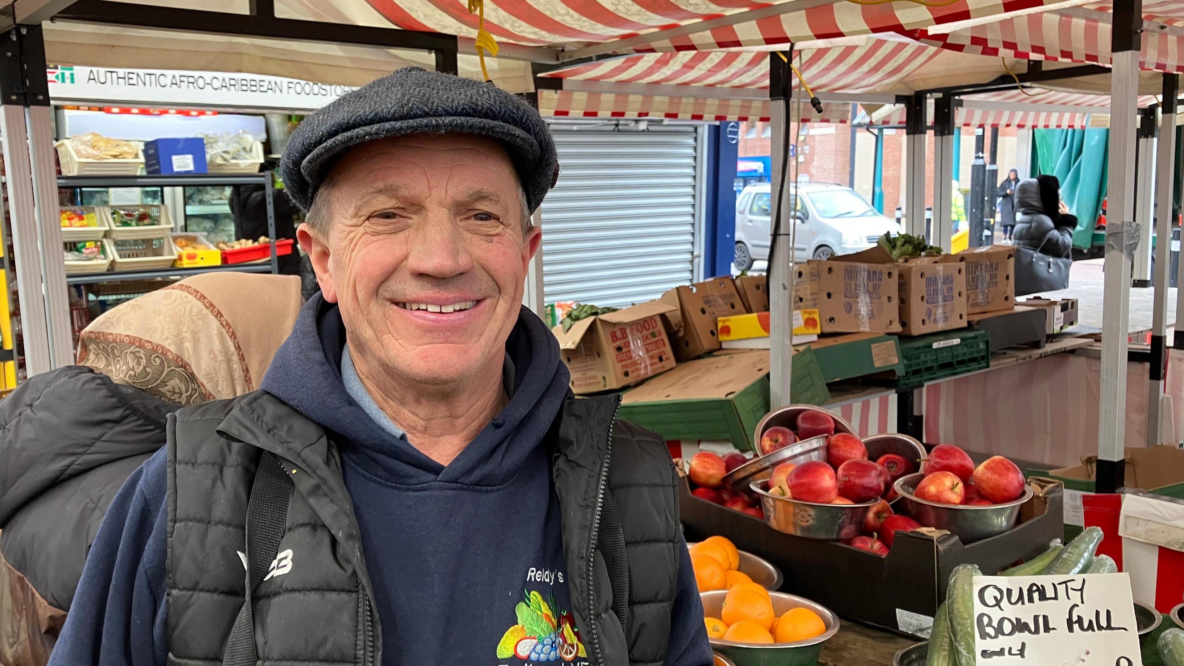 A greengrocer stood in front of apples and oranges in silver bowls