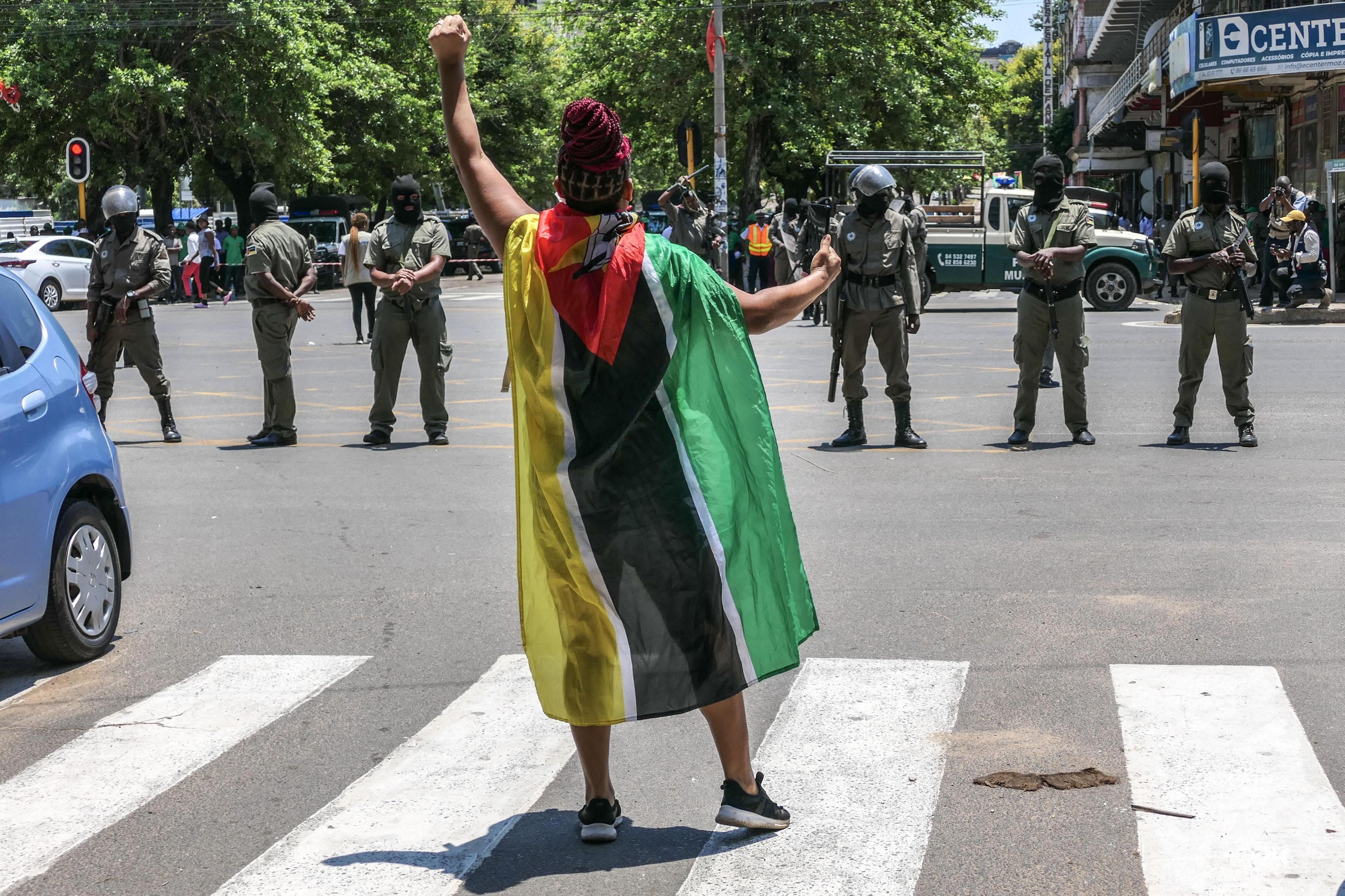 A woman draped in the Mozambique flag squares up to a line of armed policemen and shouts slogans near the Independence Square during the inauguration of Mozambique's fifth president, Daniel Chapo, in Maputo.