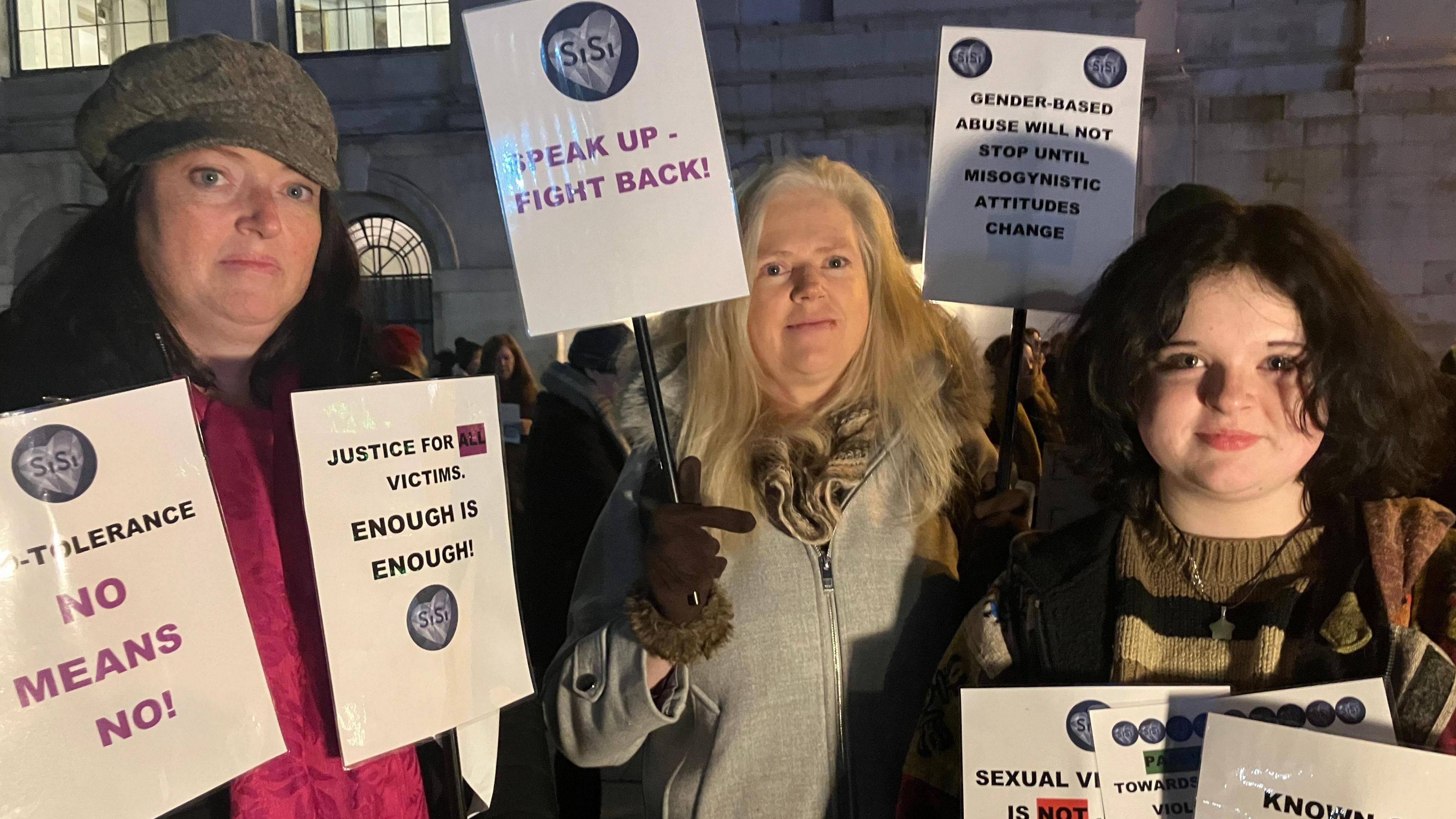 Four women stand on a winter's evening in Dublin, as part of a rally in support of Nikita hand who won a civil case against Irish mixed martial arts (MMA) fighter Conor McGregor. they are holding signs that read' enough is enough' and 'justice for victims