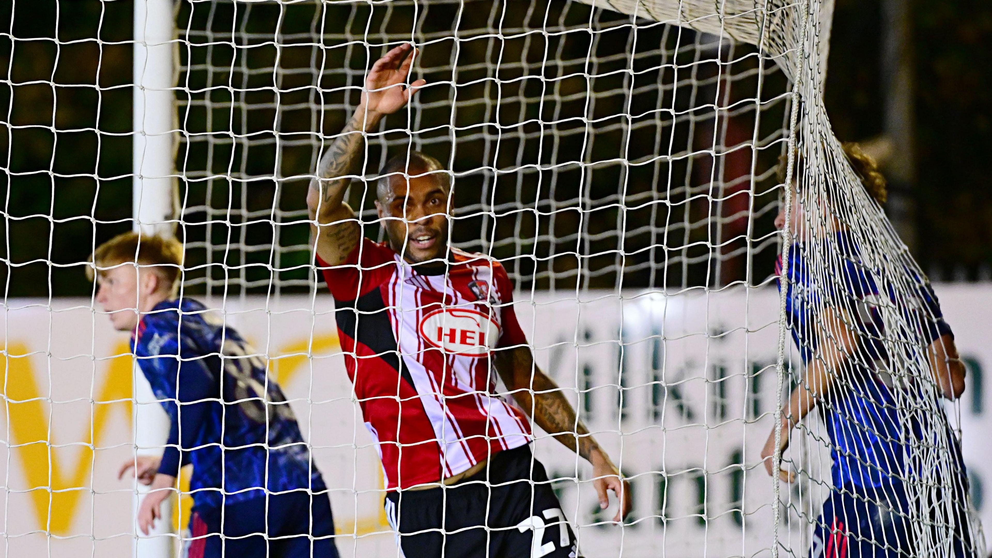 Josh Magennis, obscured by the netting, raises his arm in celebration after scoring the equaliser against Arsenal's Under-21s