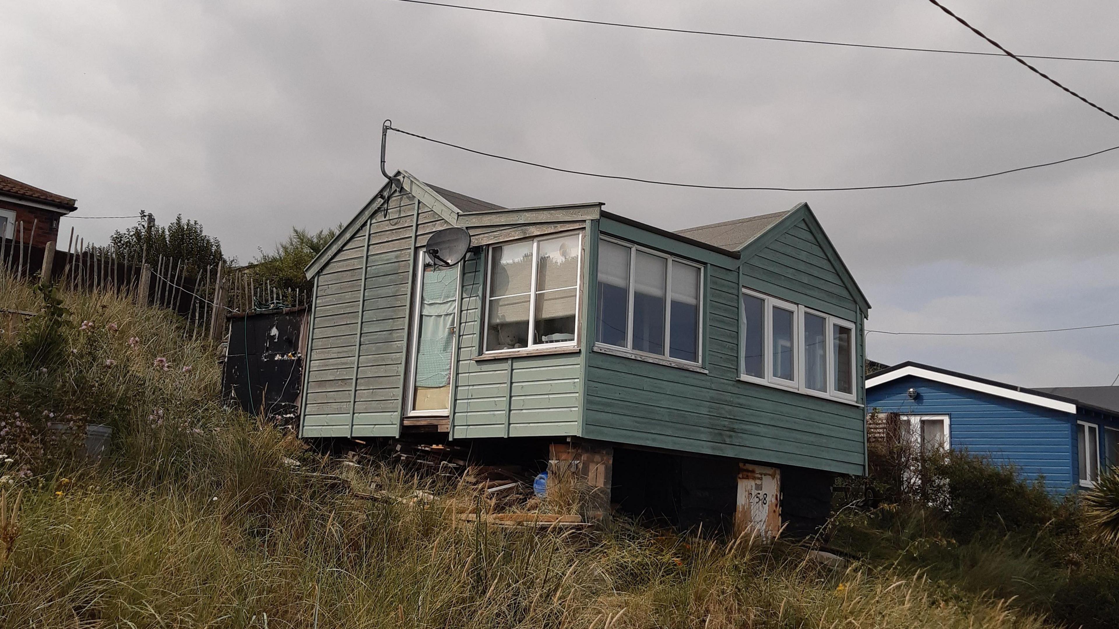 Andy Sloan's green challet perched on a grassy dune. A blue chalet is in the background.