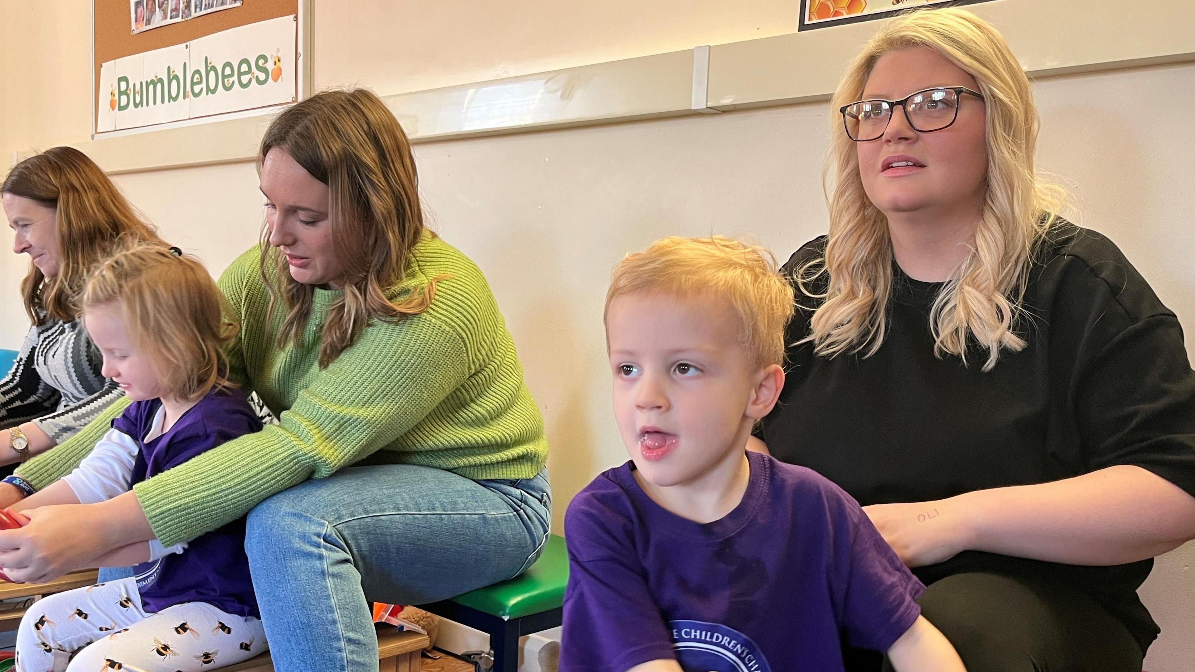 Parents and children enjoying a therapy session in a playgroup setting. In the foreground is a five-year-old boy wearing a purple T-shirt.