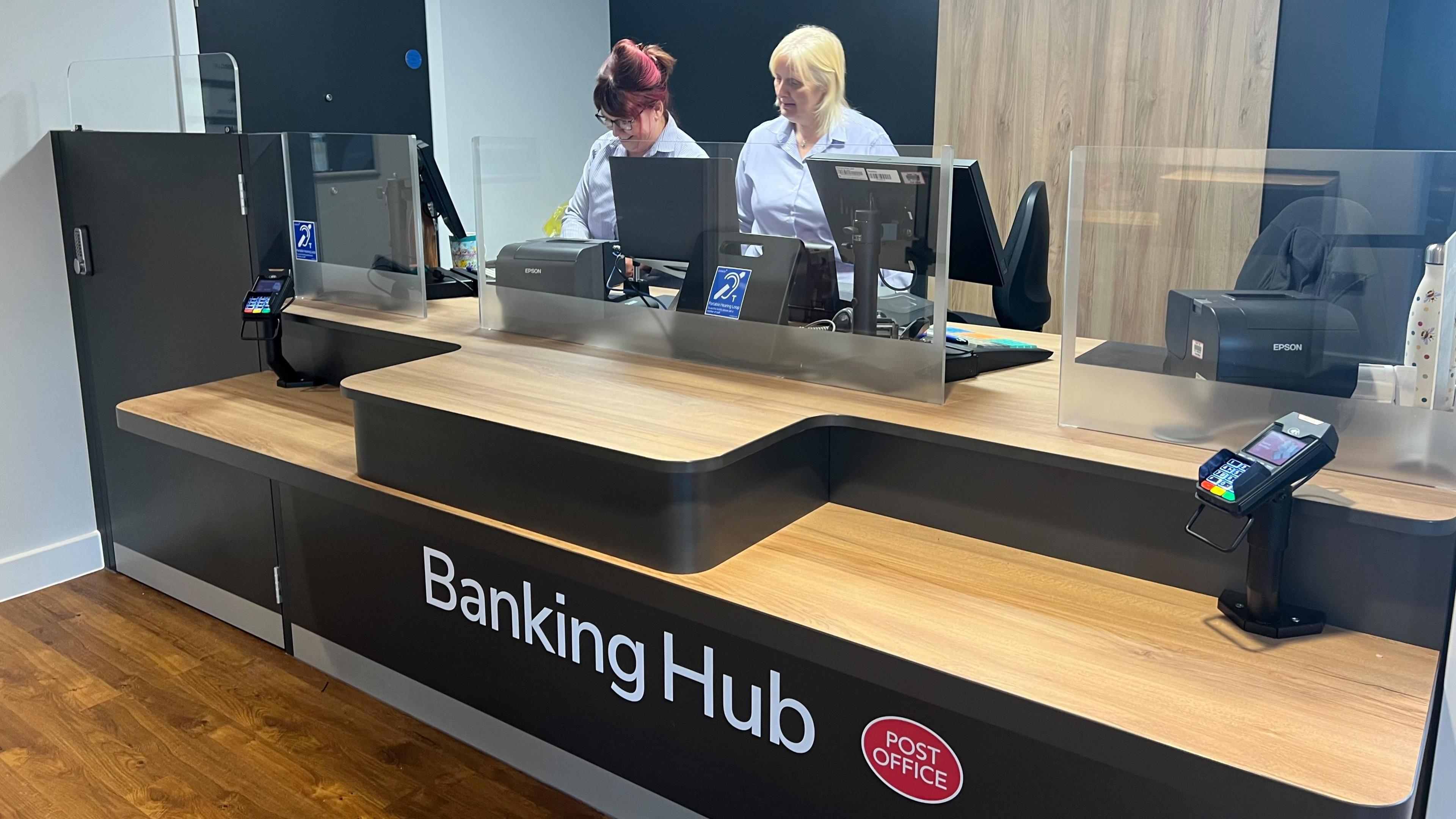 Two women behind a wooden banking counter