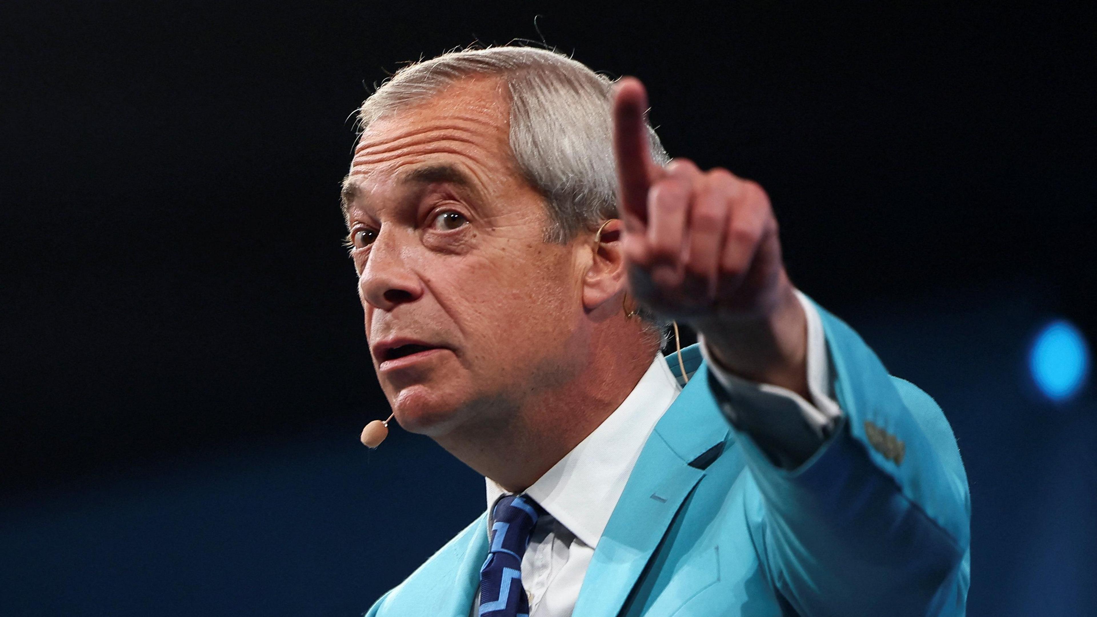 Nigel Farage speaking at his party conference and is pointing his index finger towards the camera.