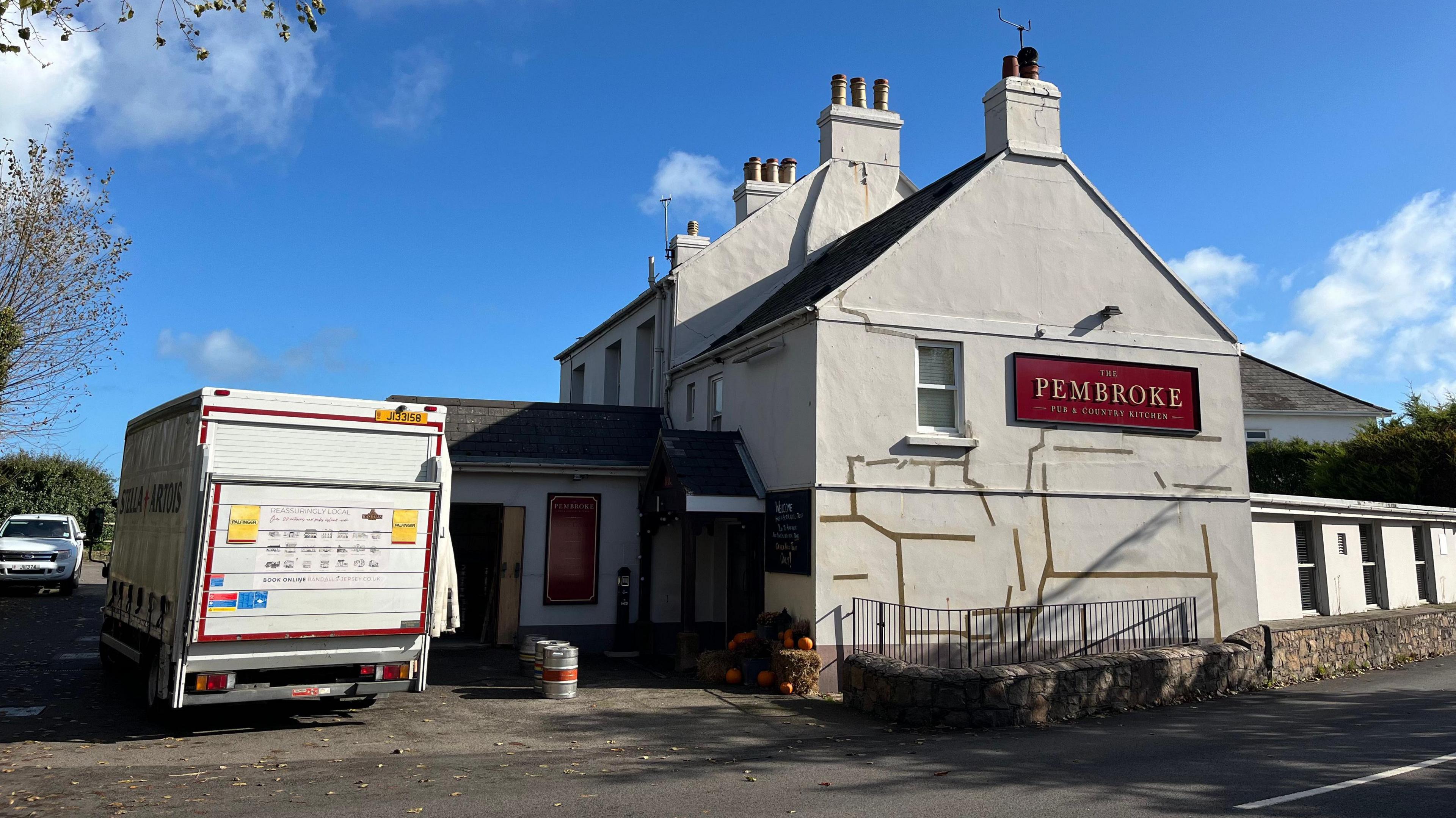 The Pembroke pub in Jersey with white walls and a red name sign. A van delivering kegs of beer is parked outside.