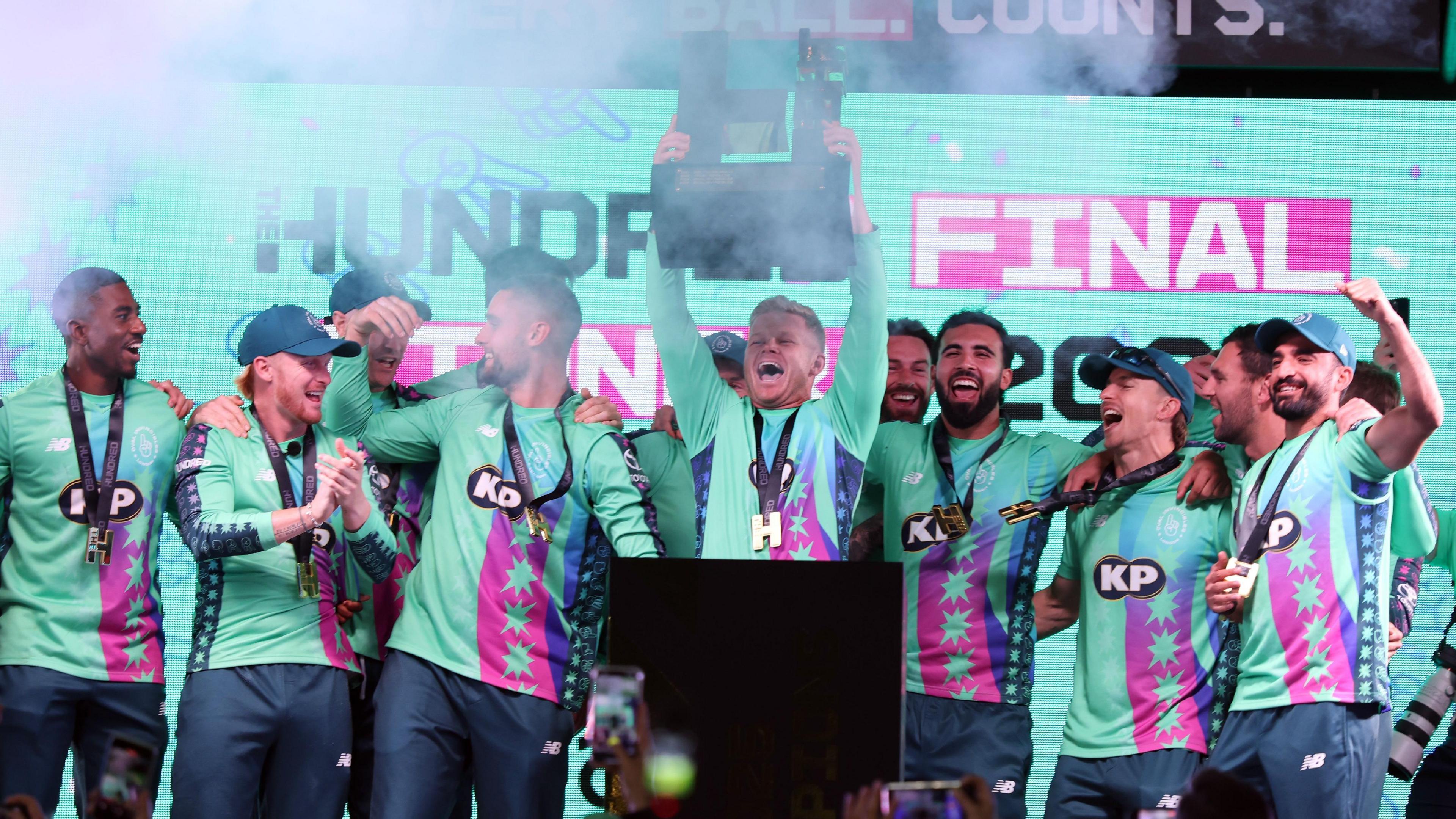 Sam Billings lifts The Hundred trophy surrounded by his Oval Invincibles team-mates.