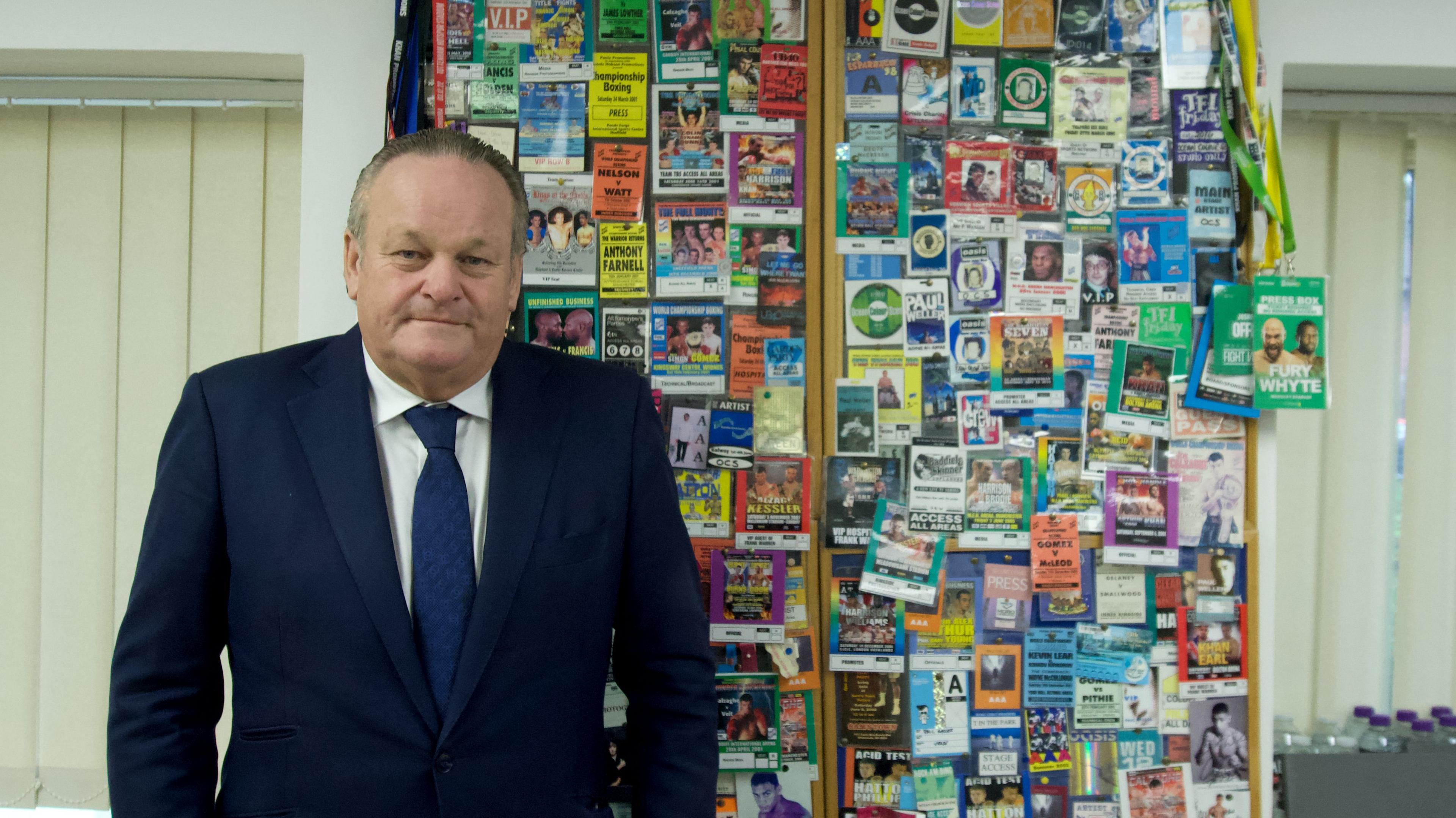 Ian McCallister is in a blue suit, white shirt, blue tie and standing next to a frame containing lanyards and security passes