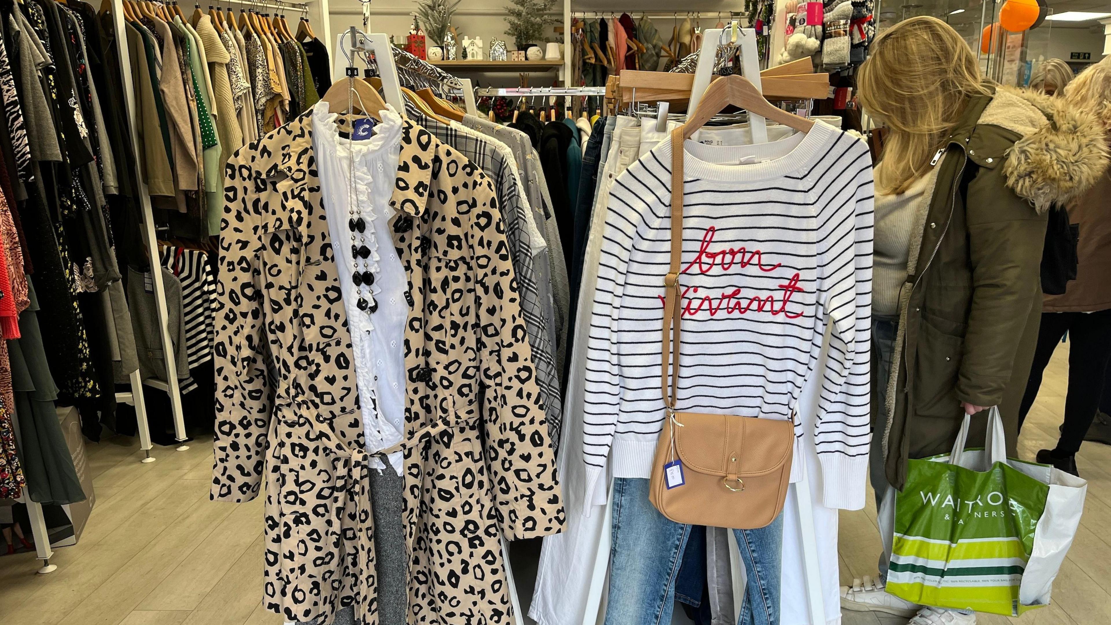 A leopard print coat and trousers on a hanger, next to a stripey sweatshirt, jeans and handbag on a hanger.
