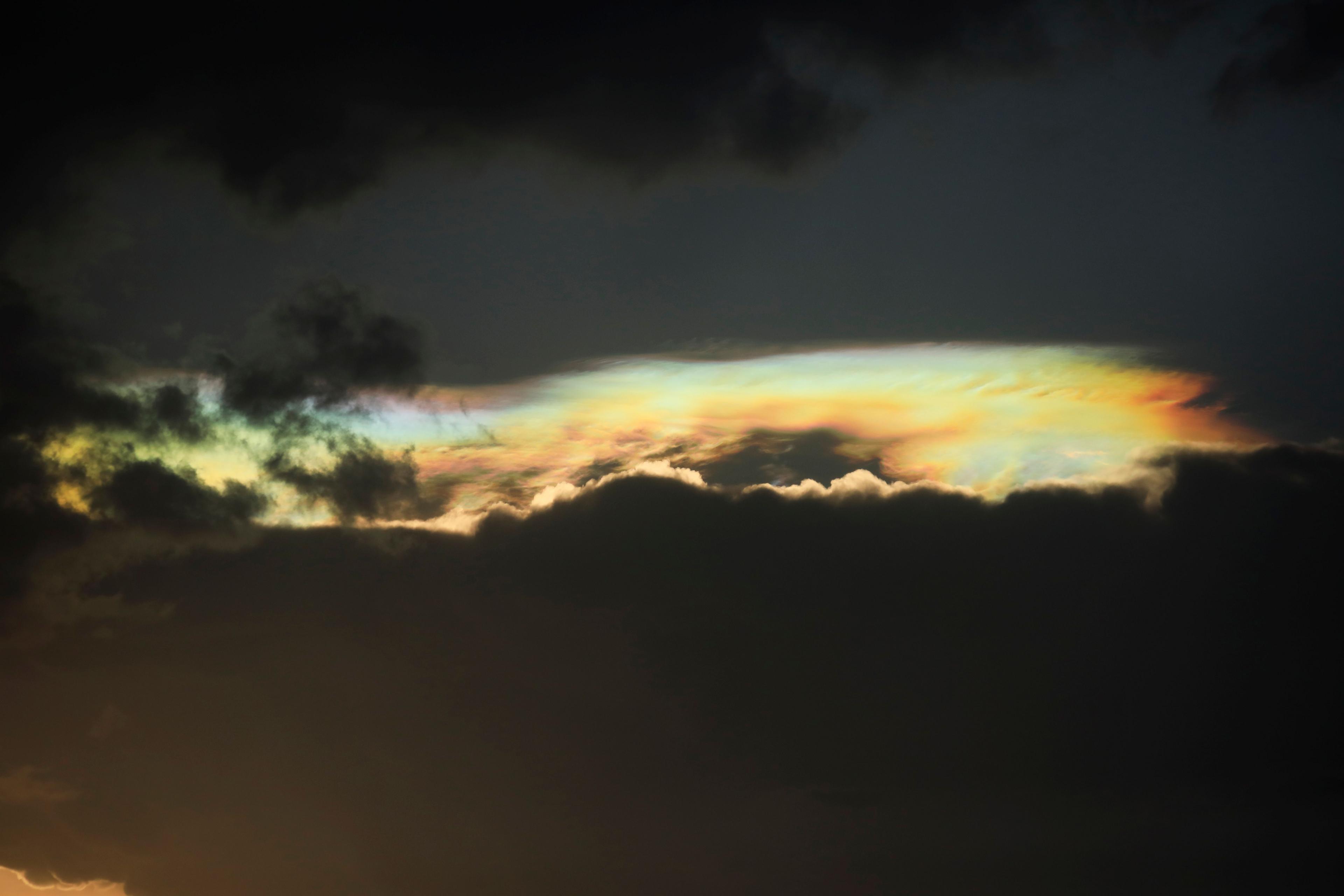 Rainbow coloured clouds can be seen through dark clouds 