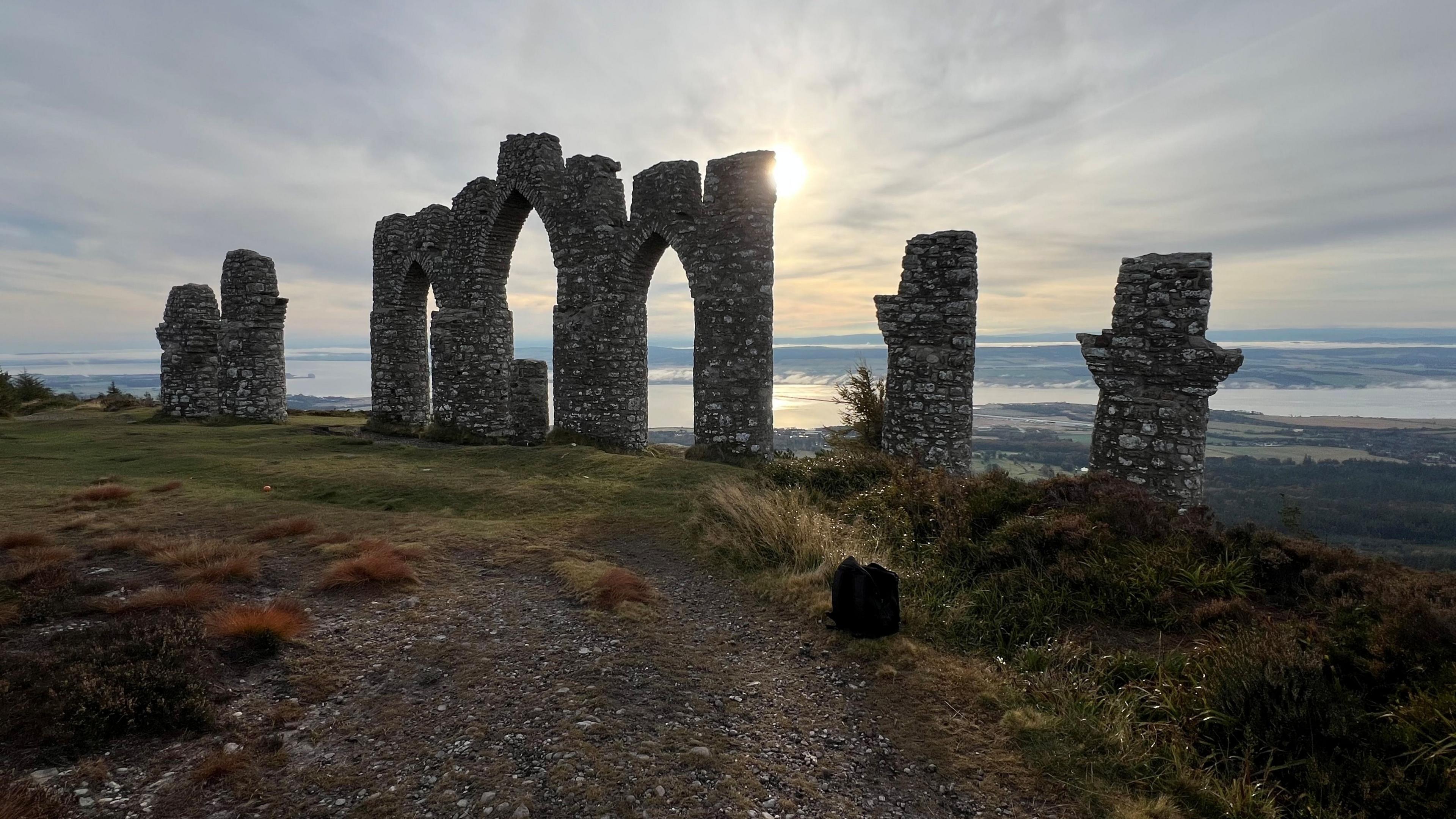 A stone monument, including a central arch shape, on a sunny hillside