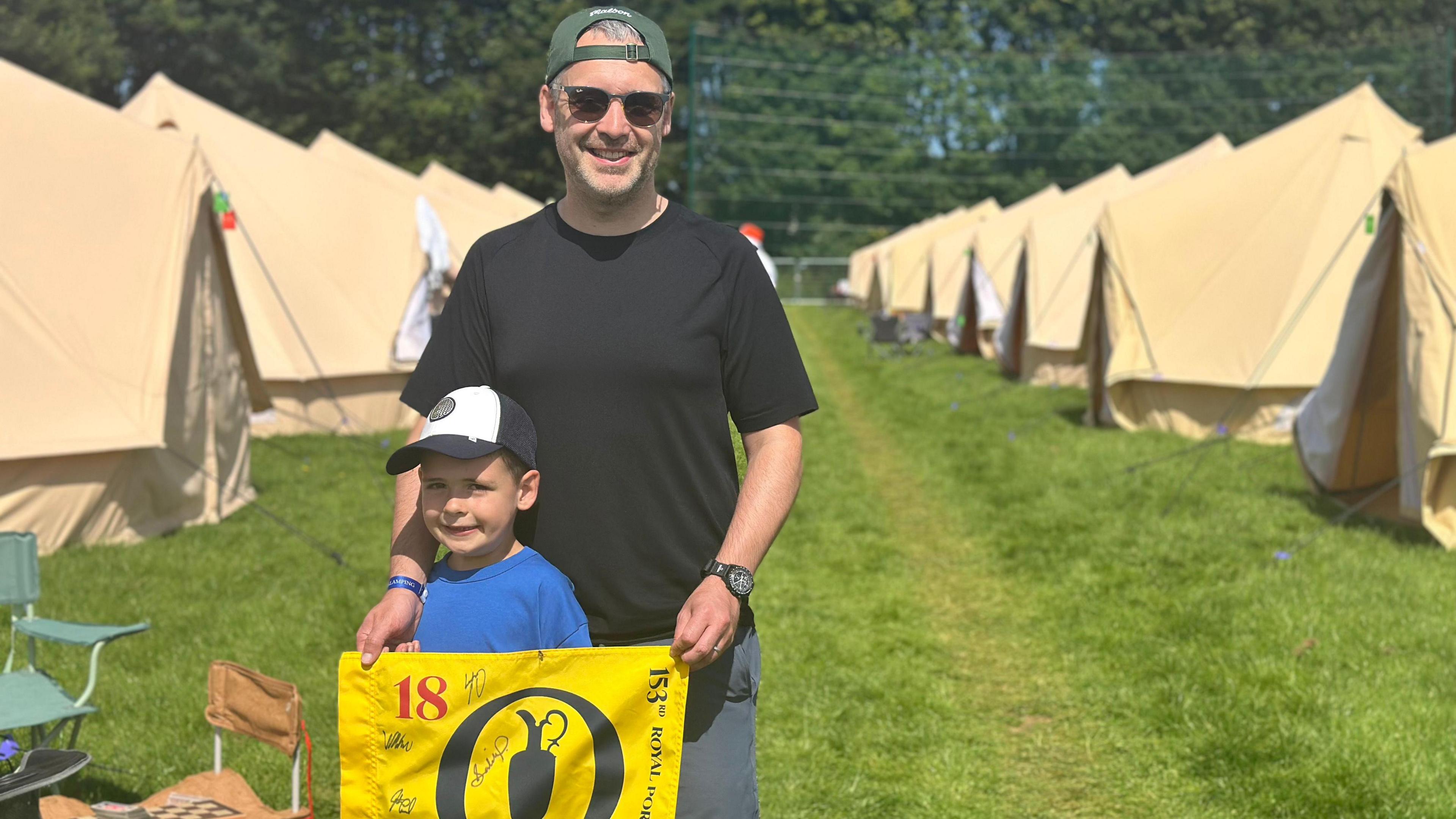 Ronan Cooper and his son, Alex, are seen at the campsite holding a yellow flag that has a number of signatures on it.