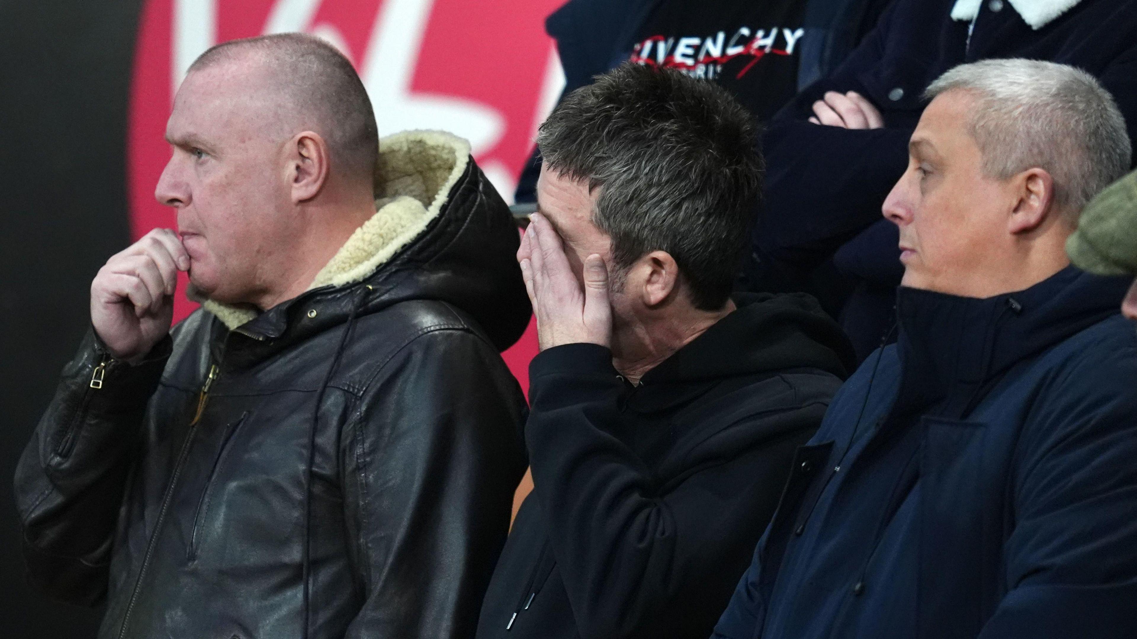 Noel Gallagher with his hand over his forehead, standing in the crowd at Bournemouth Vitality Stadium.