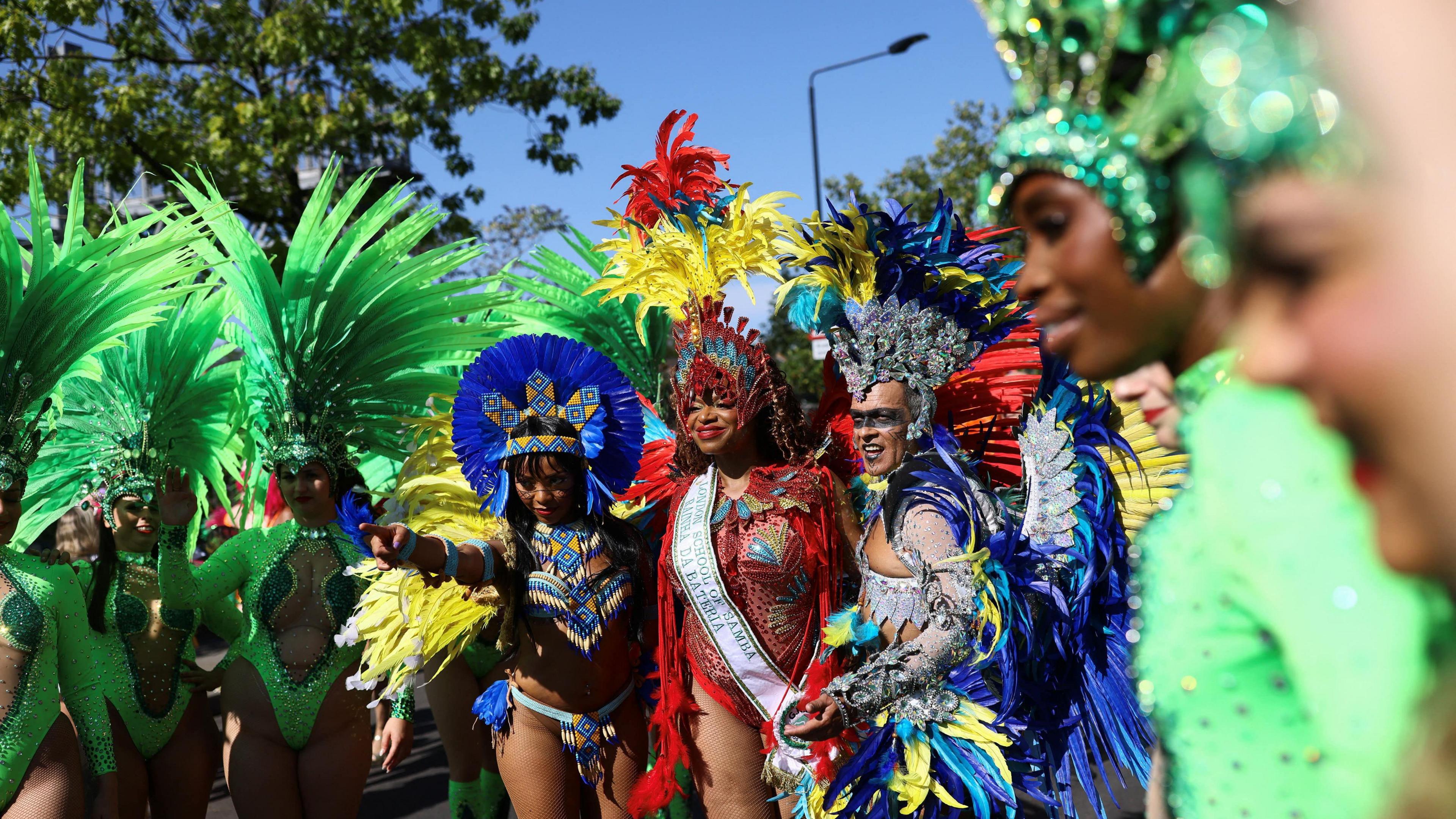 A group of people in green, blue and red costumes with feathers stand together. 