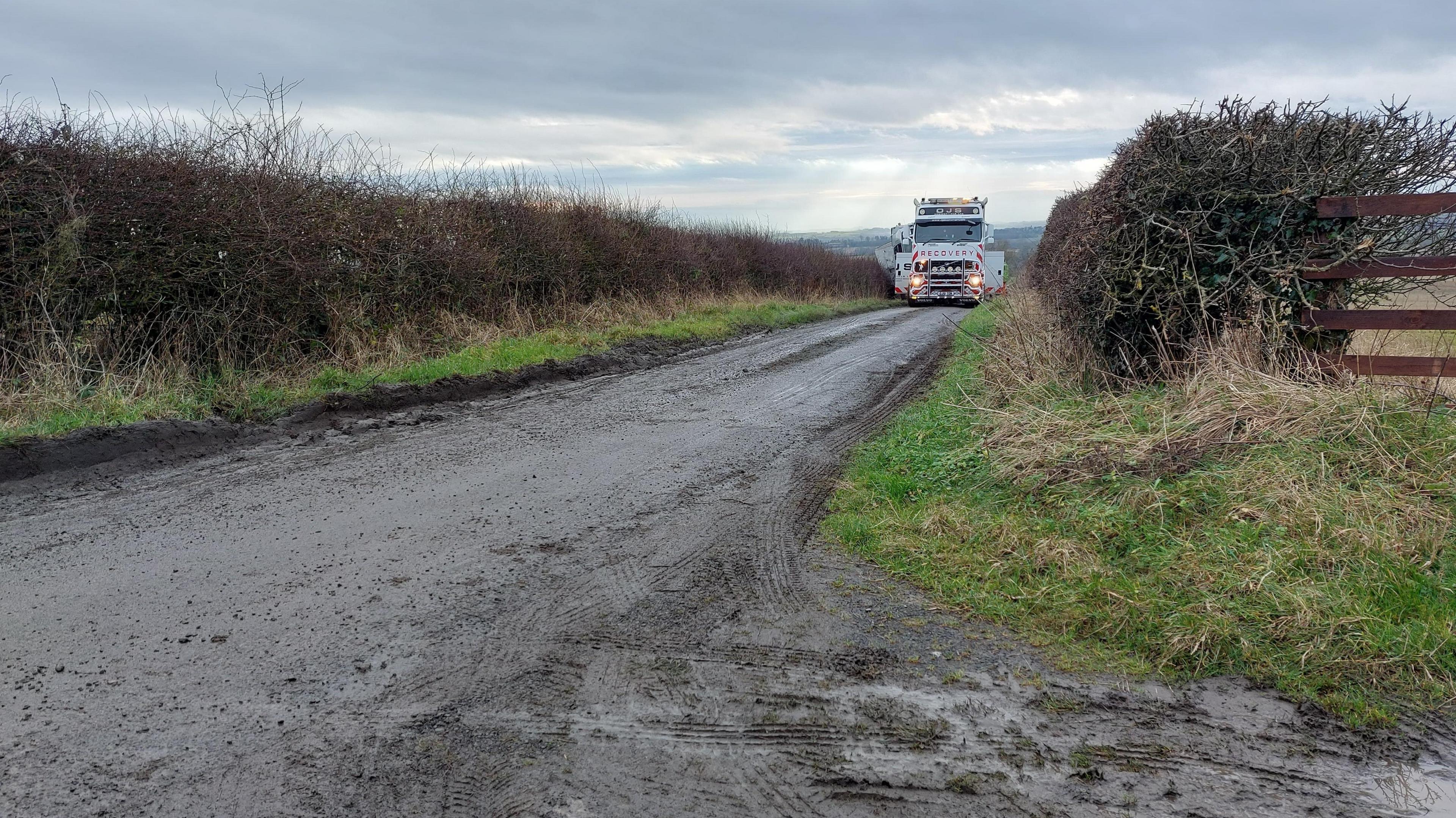 A lorry makes its way slowly along a narrow country lane.