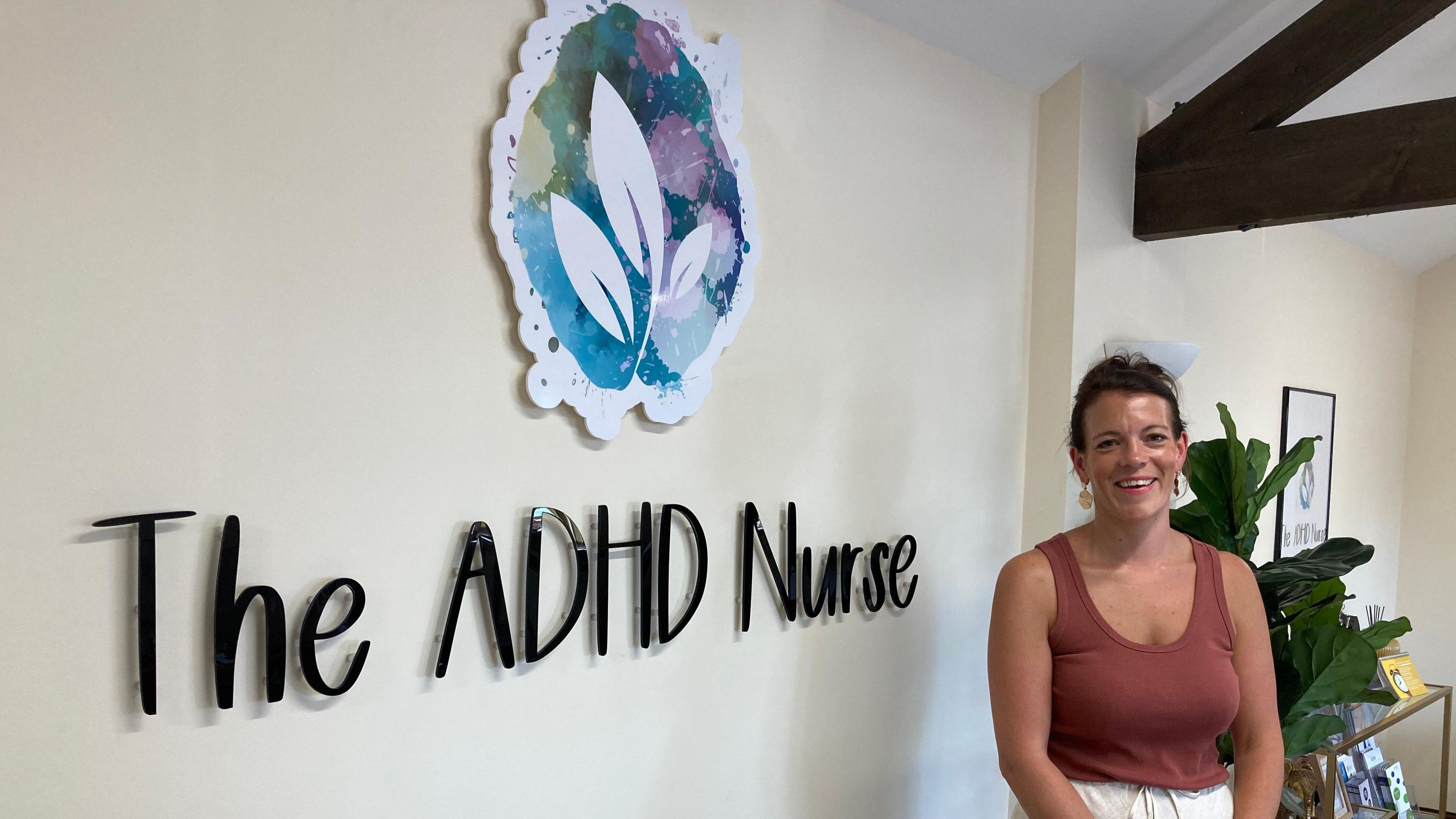 Vicki George stood in red top and white shorts near wall sign saying 'The ADHD Nurse'