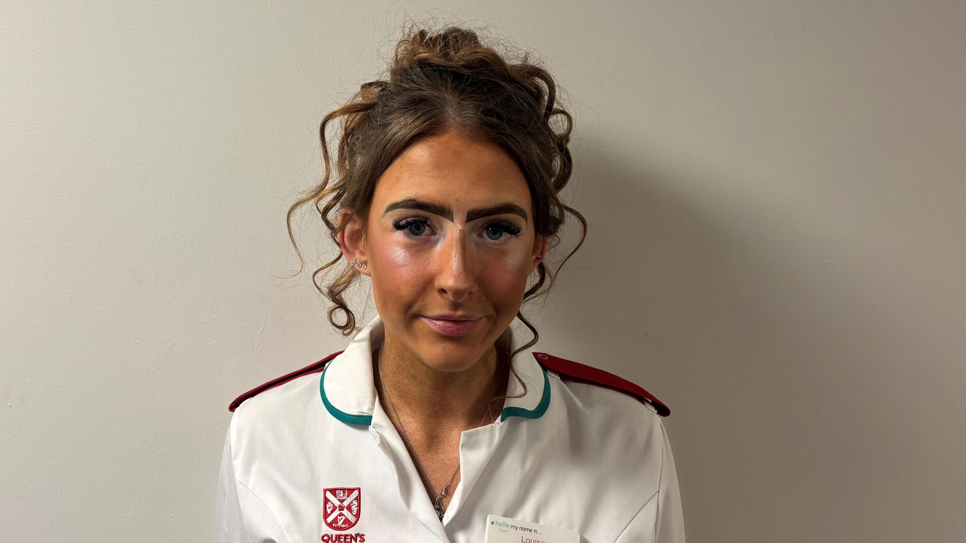 Louise Bradford is wearing a white nurses uniform. She has brown hair. She is in front of a white background.