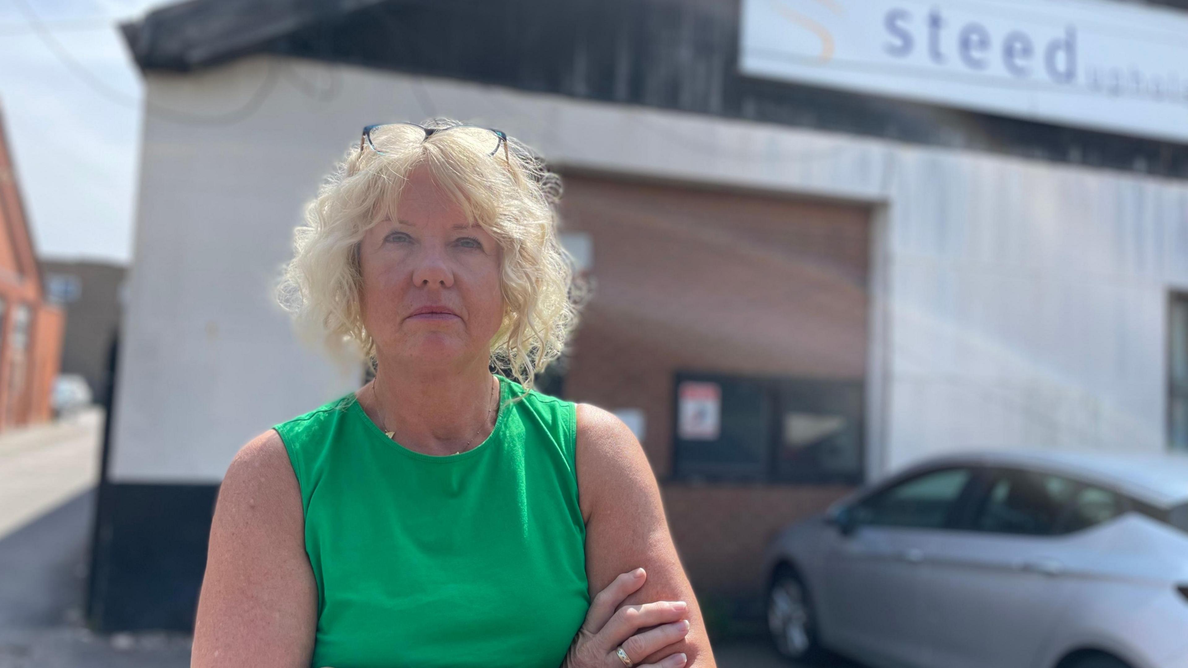 A woman with crossed arms looking irked outside a factory building