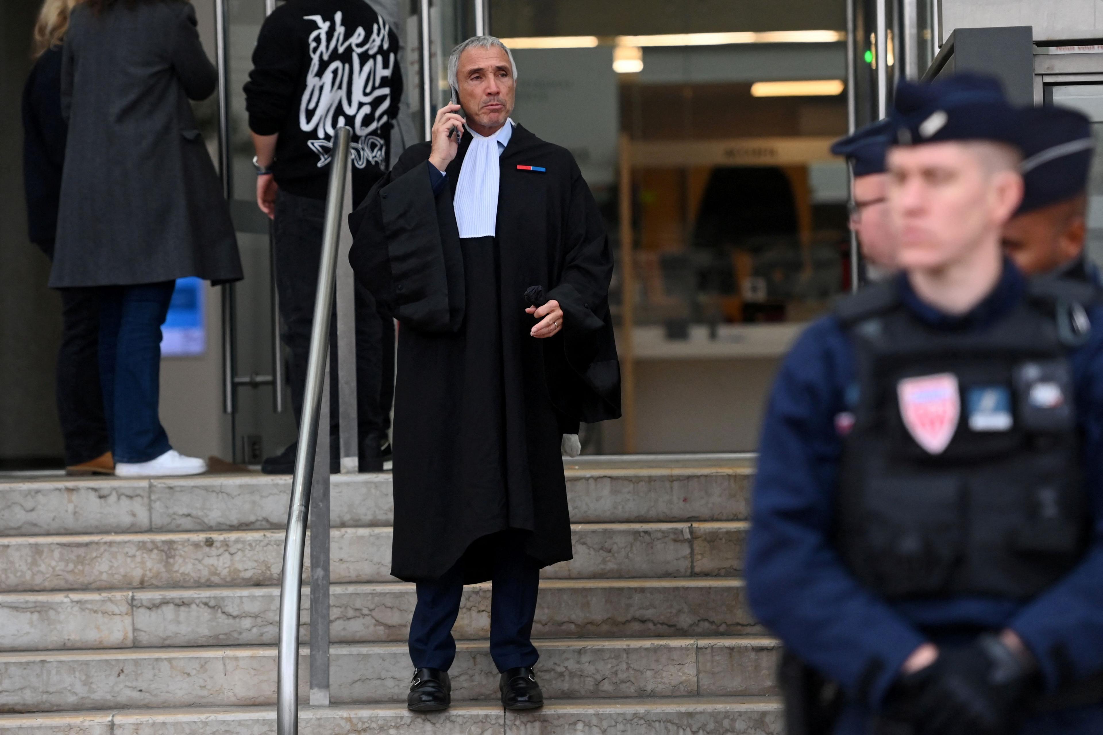 A man dressed in lawyer's robes stands on the steps of a tribunal, talking on the phone