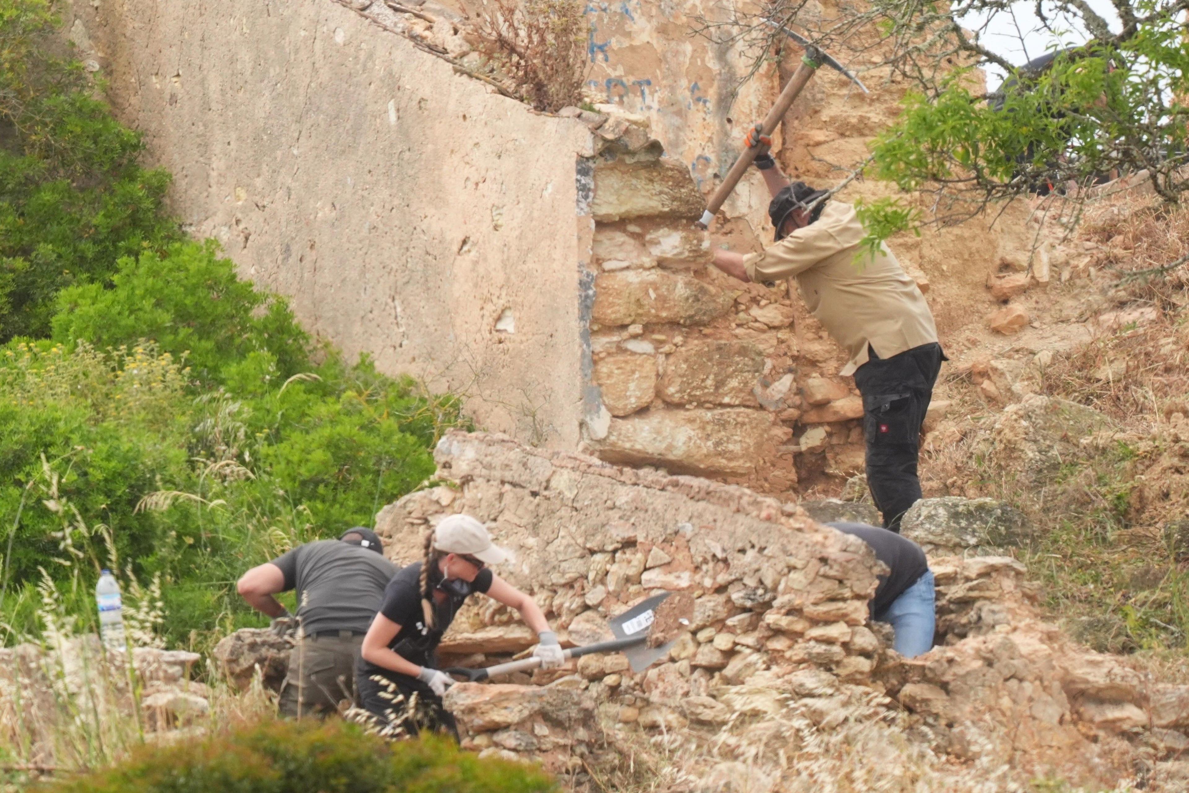 A search team uses spades and pickaxes to move rocks and dirt outside an abandoned building.
