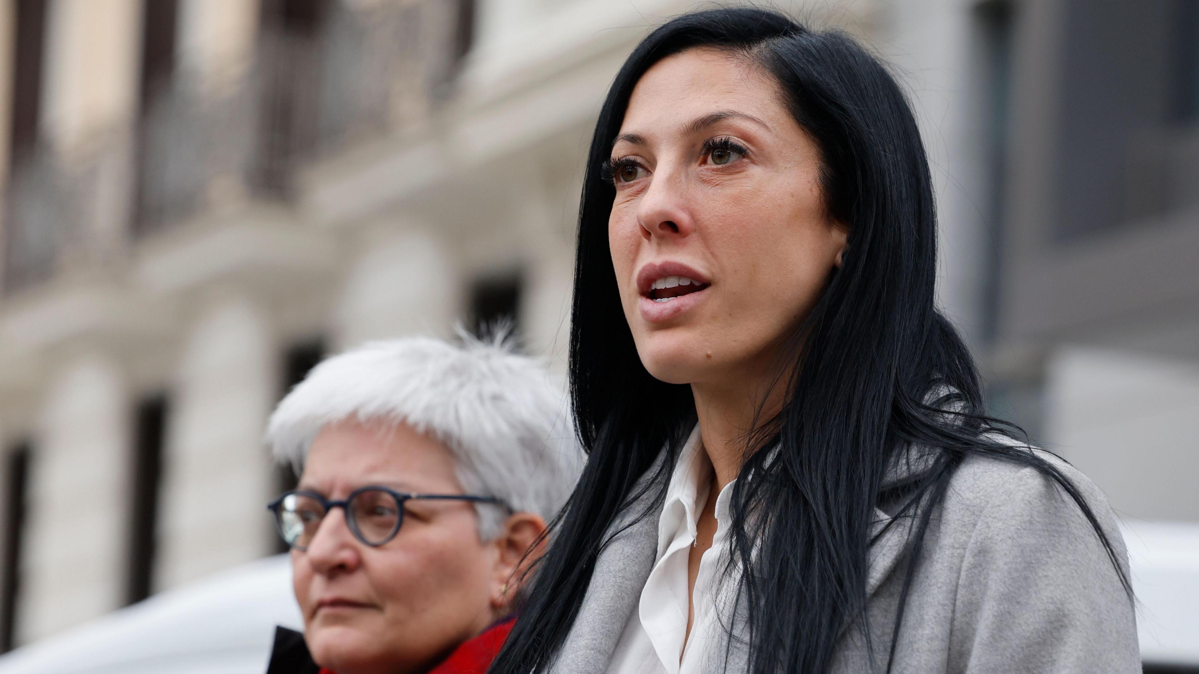 Jenni Hermoso, a woman with long black hair and brown eyes, wears a grey coat and white shirt.