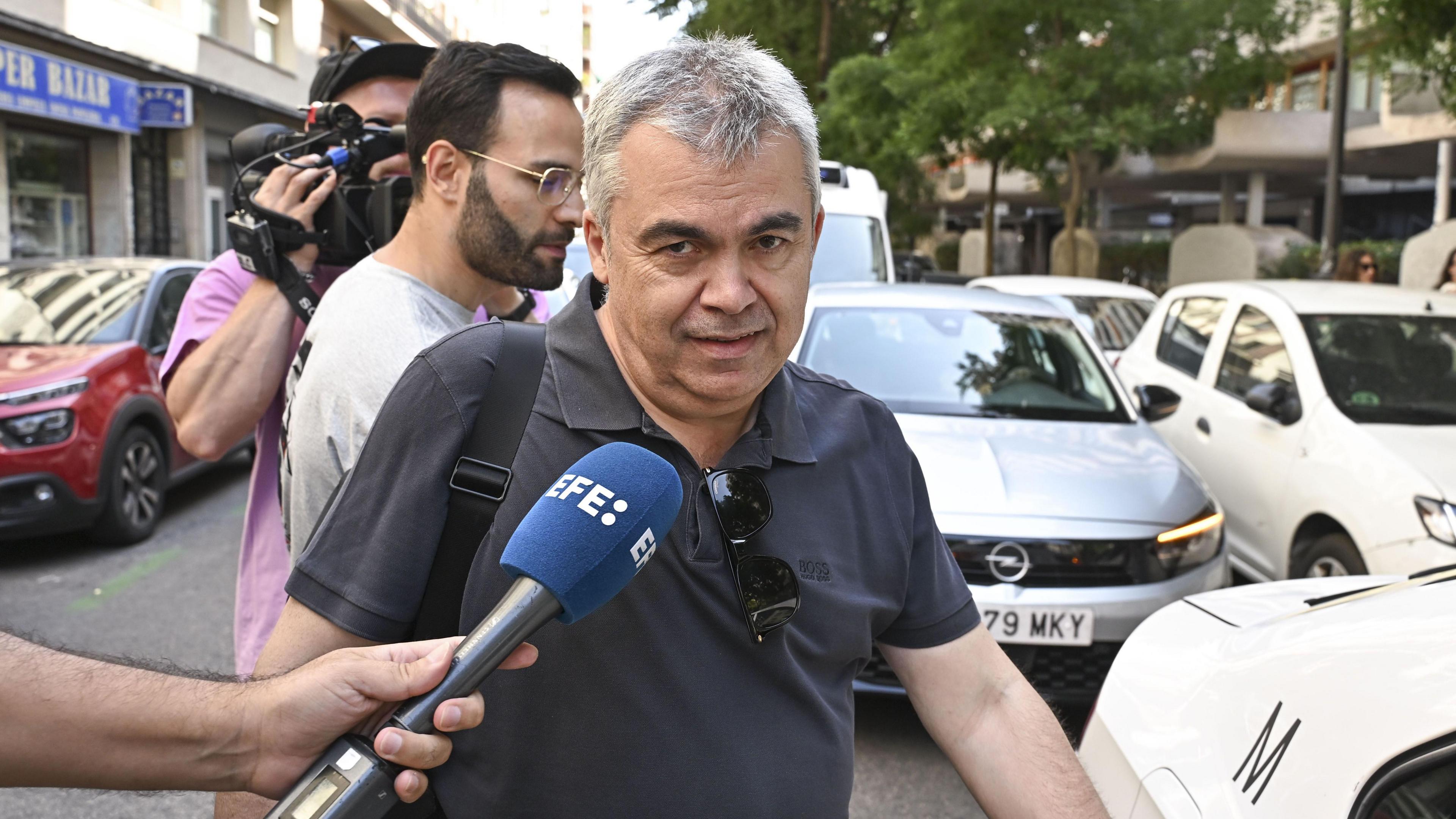 Santos Cerdán is being doorstepped by journalists. He is looking into the camera and a journalist is holding a microphone to his face.