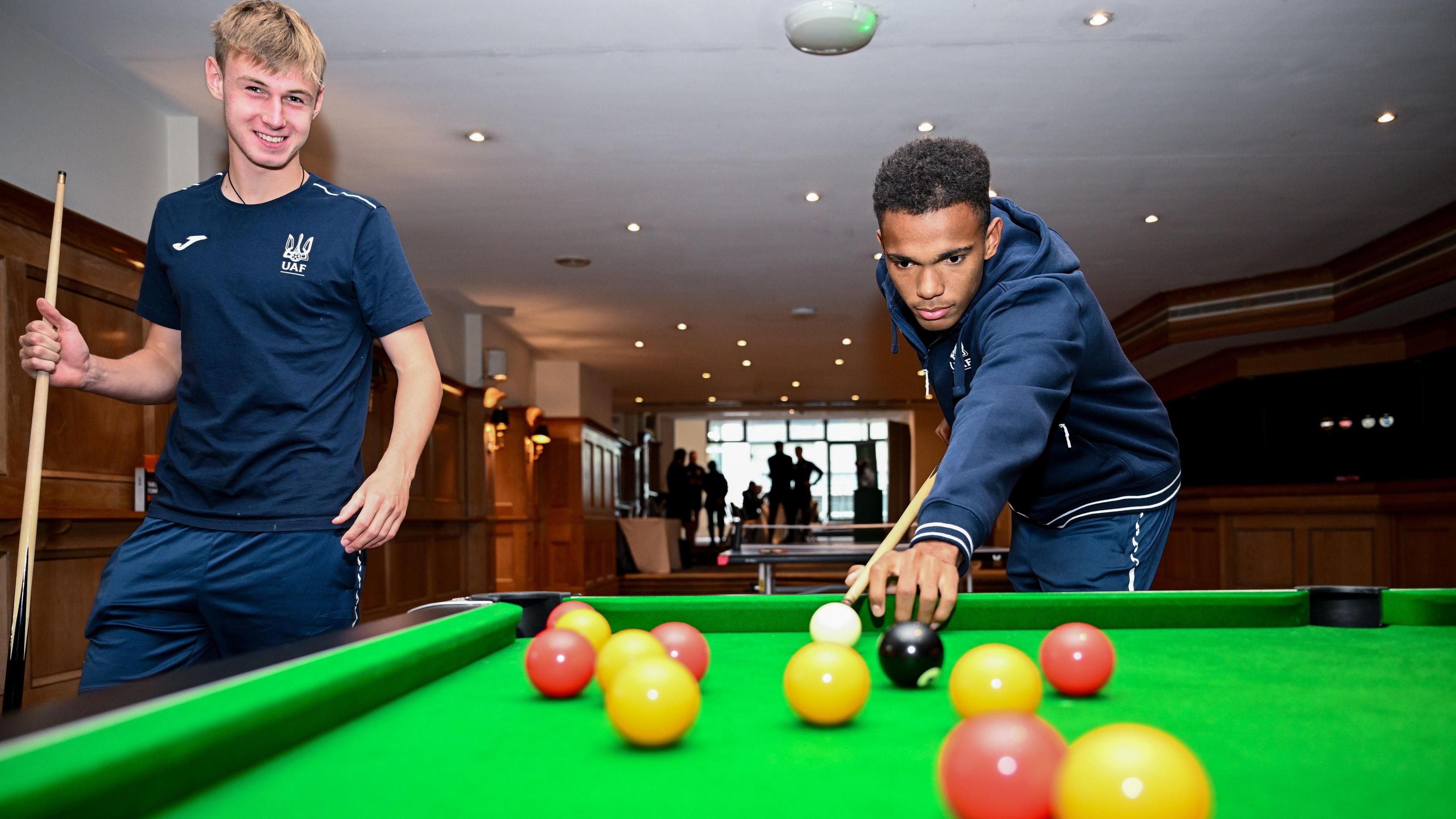 Ukraine players playing pool in a hotel setting wearing dark blue team outfits 