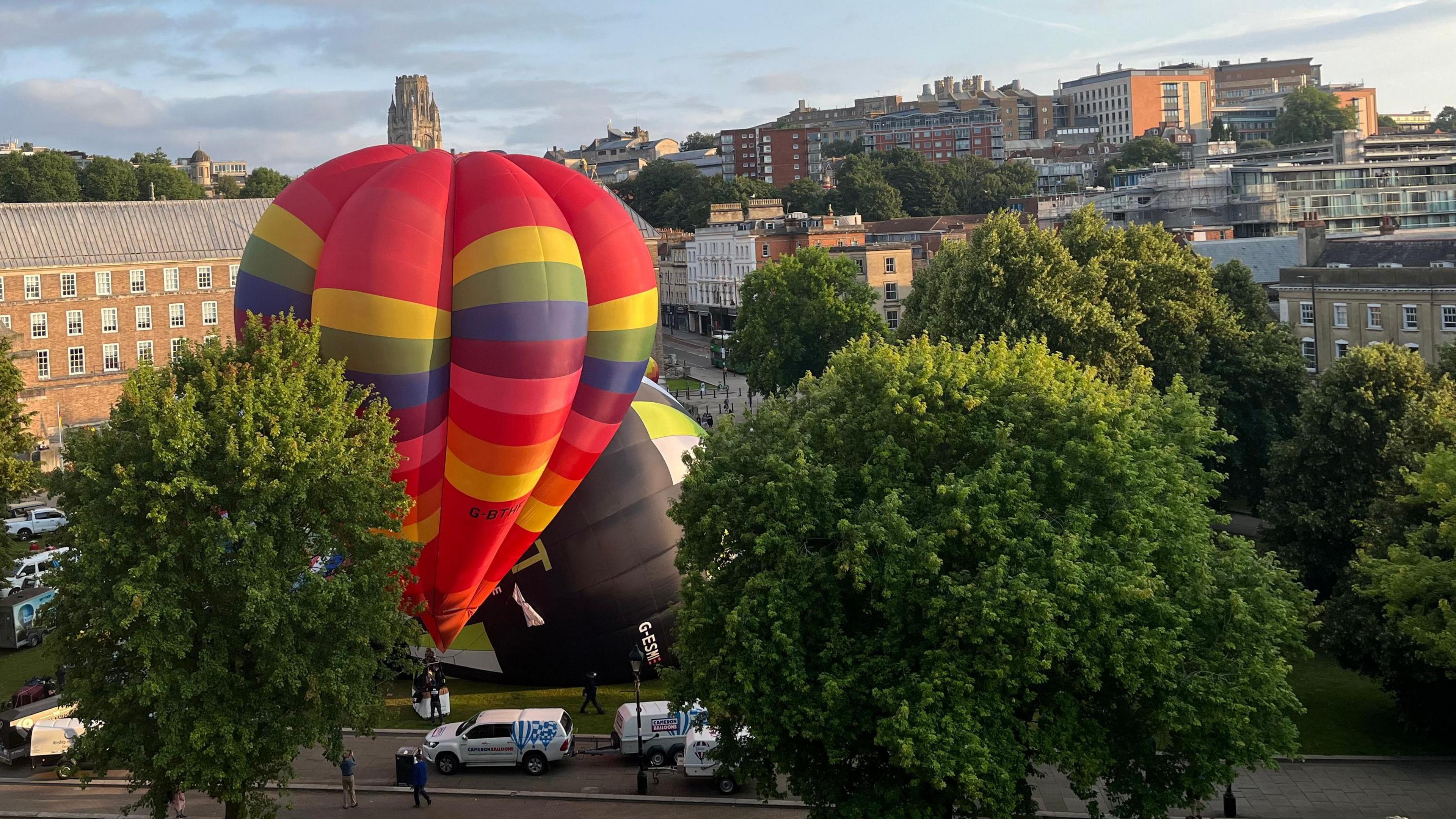 A large pink hot air balloon with rainbow stripes tethered to College Green