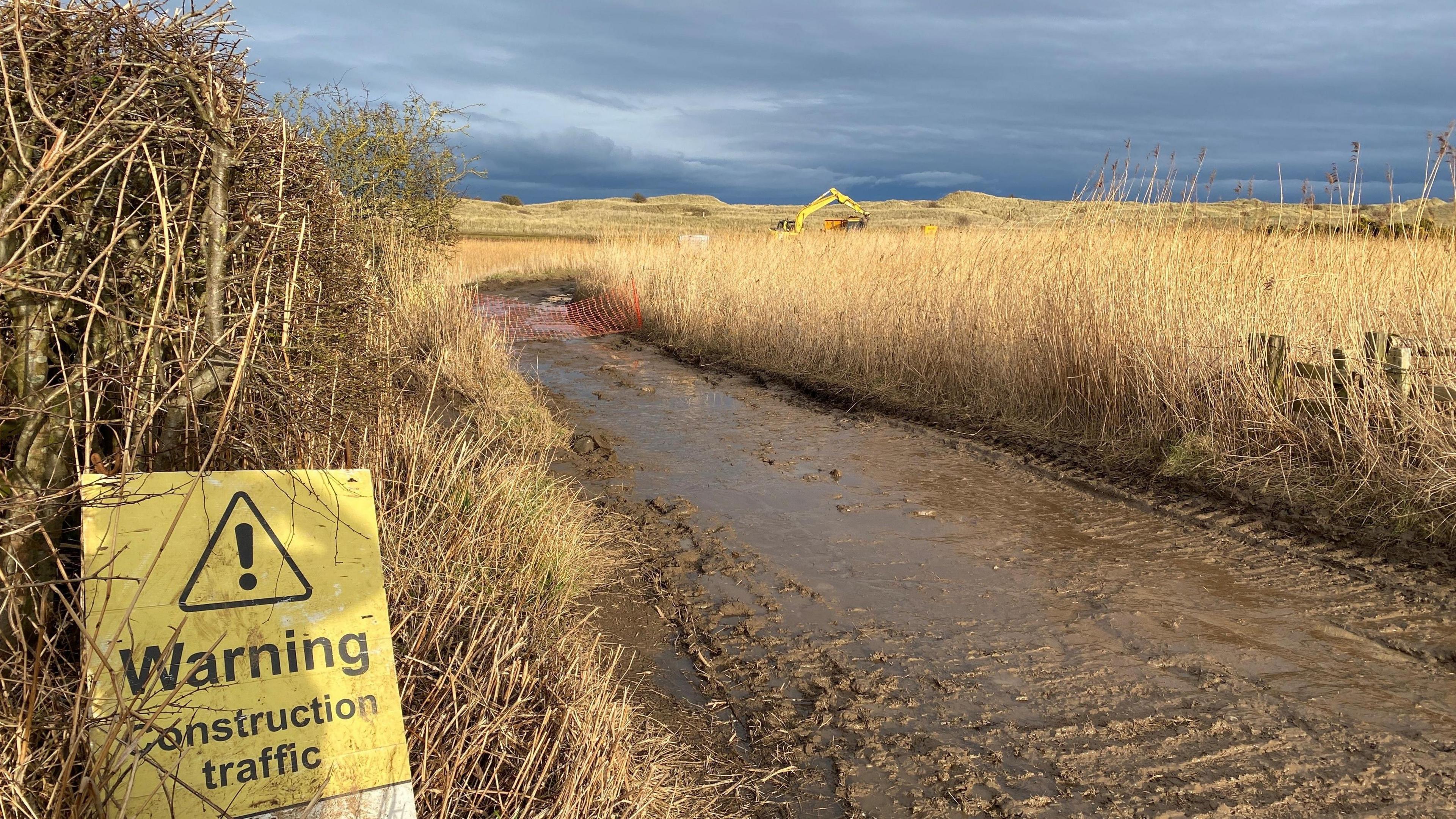 A yellow sign reads: "Warning. Construction traffic." It sits in vegetation alongside a very wet and muddy track.