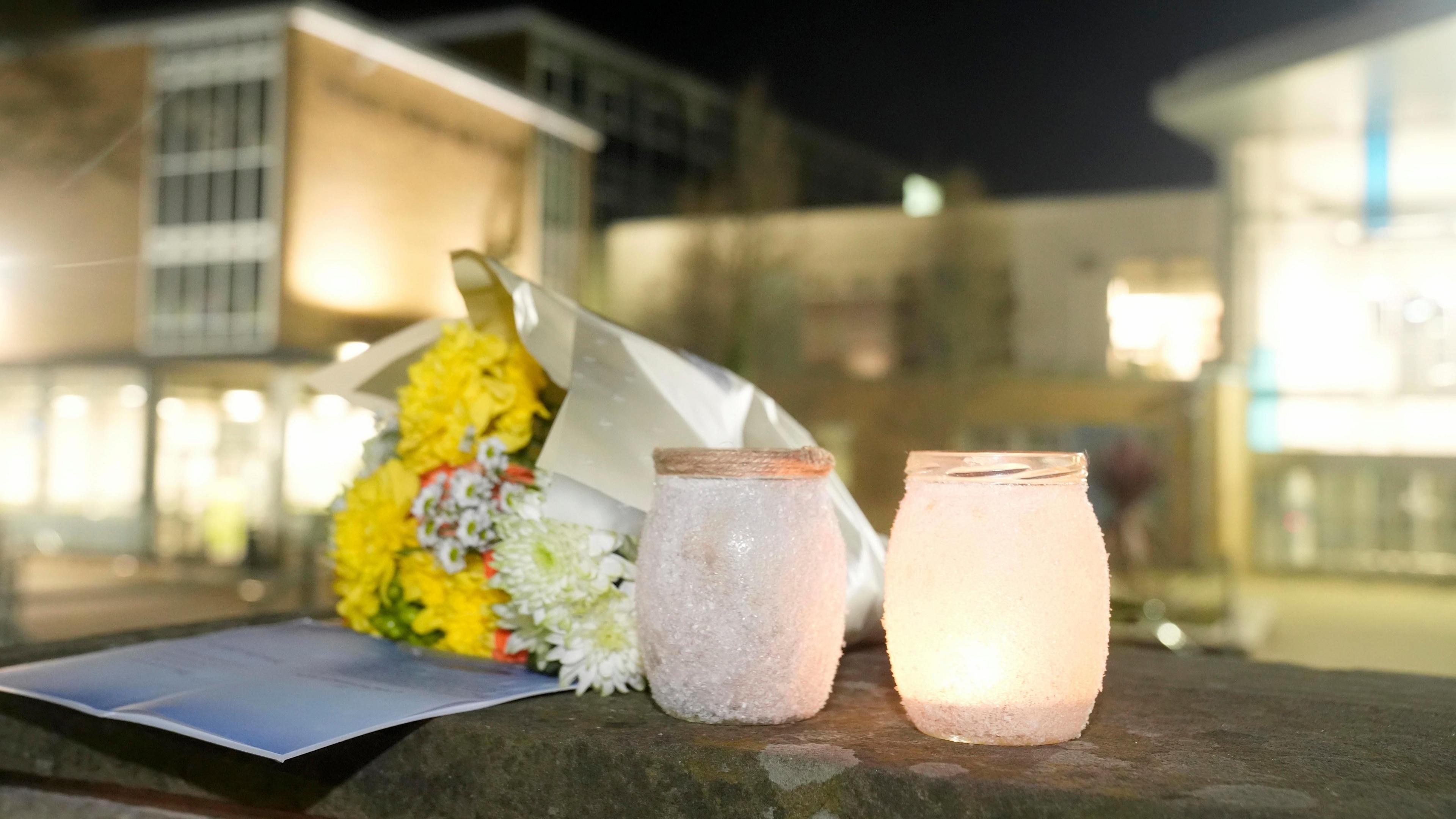 Two lit candles, a bunch of flowers and a card are left on a wall outside All Saints Catholic High School, on Granville Road in Sheffield