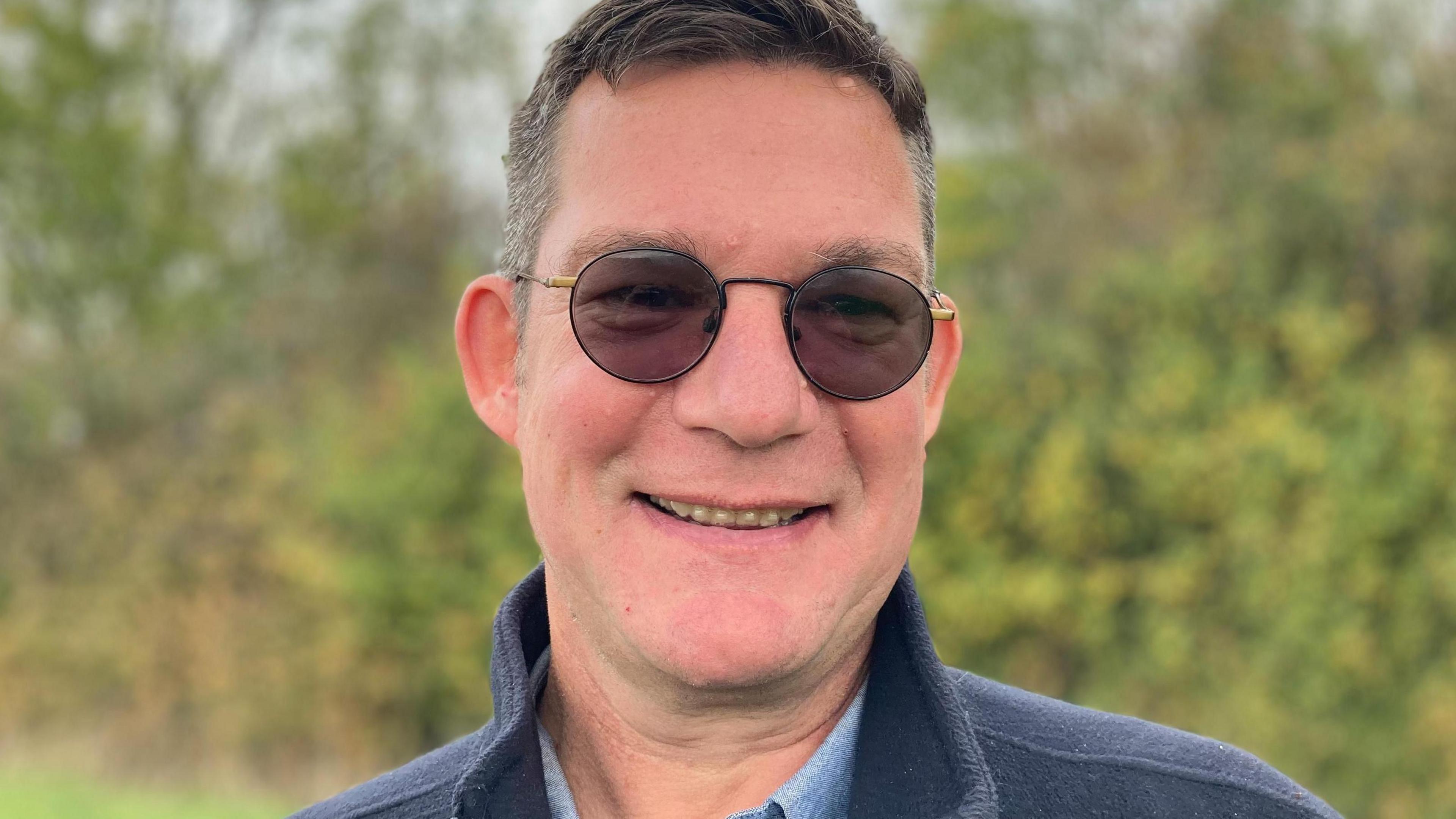 Man with glasses and dark hair wearing a dark blue fleece and blue shirt