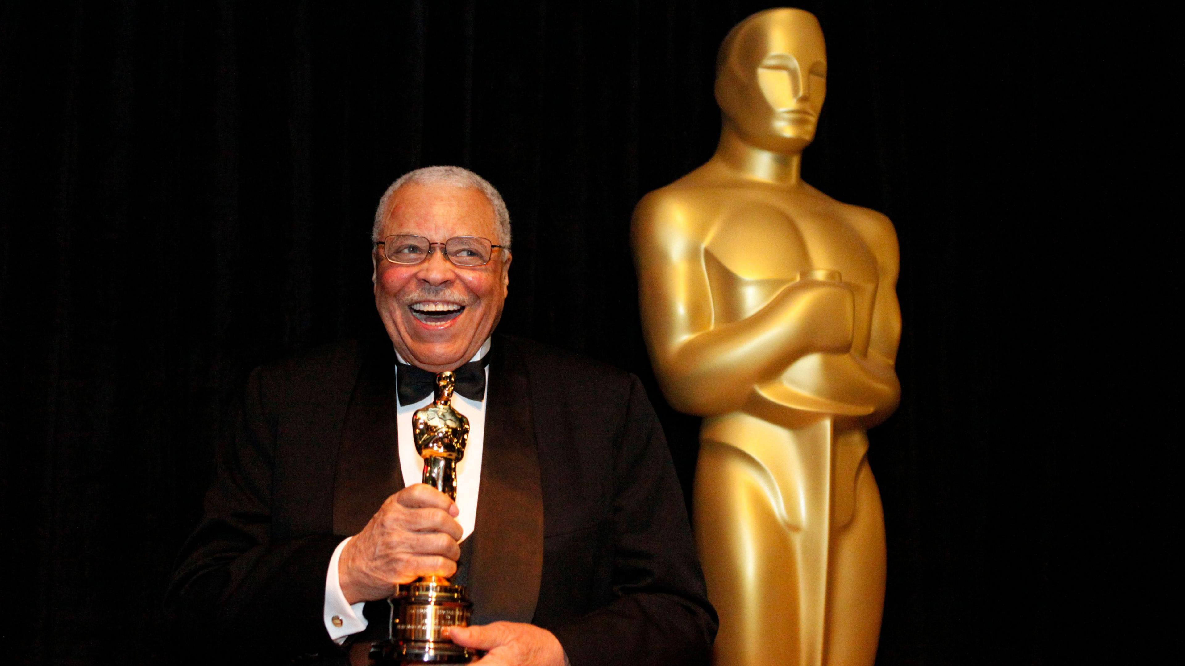 Wearing a black and white tuxedo with a black bow tie James Earl Jones smiles clutching his honorary Oscar next to a statue of an Oscar Award. This was taken at the 84th Annual Academy Awards show in Los Angeles in February 2012.