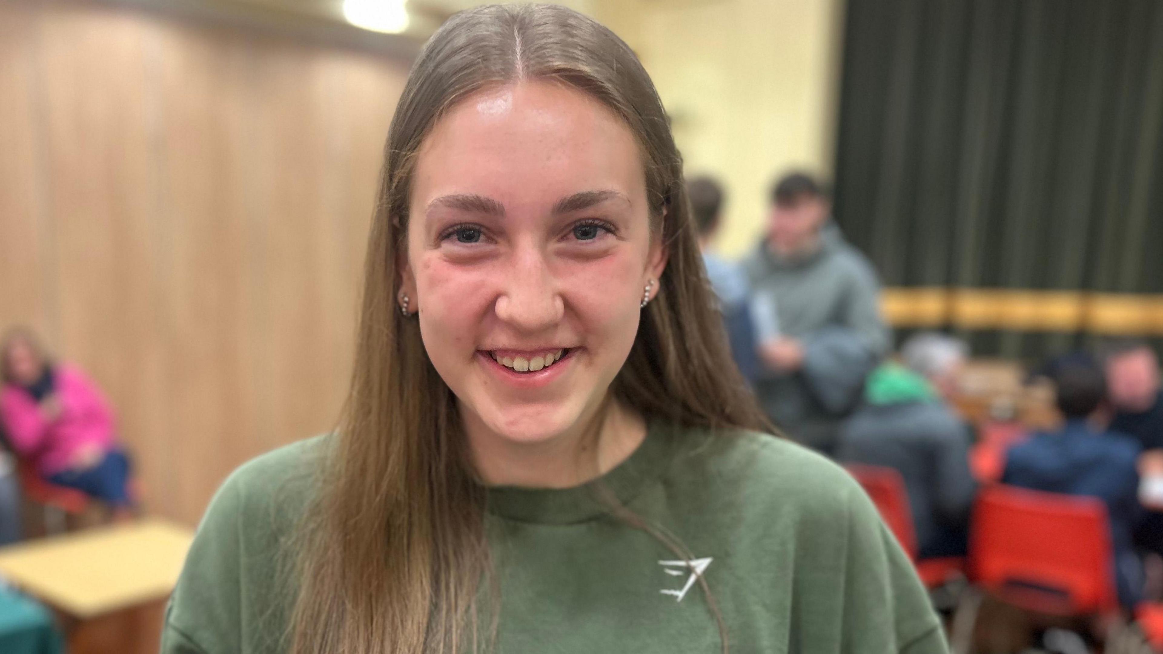 Ruby, a 16-year-old girl smiling excitedly at the camera with other students in the background.