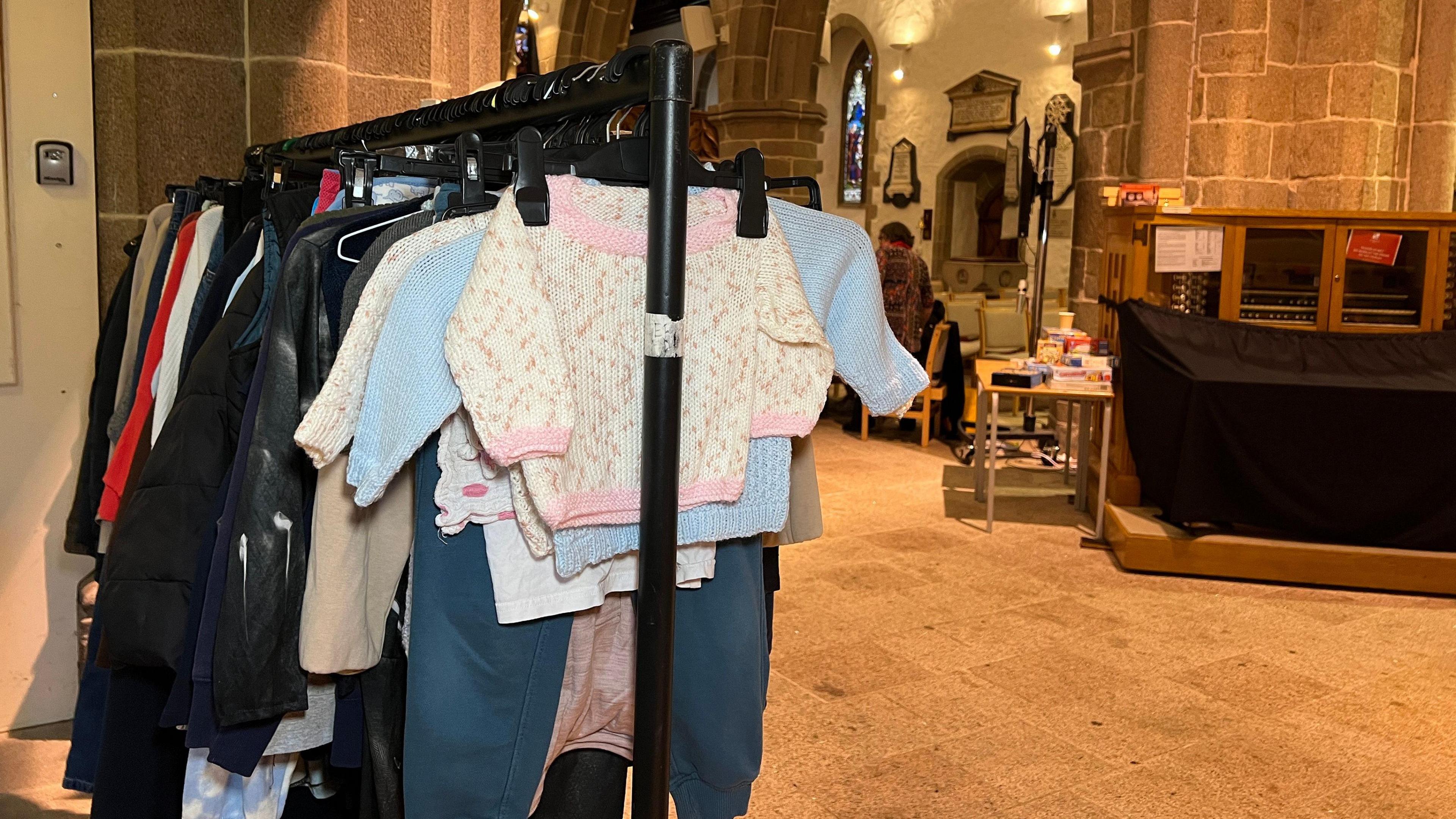 Baby jumpers are hanging from the front of the rail while clothes for older people are hanging behind them. To the left - is the Town Church hall.