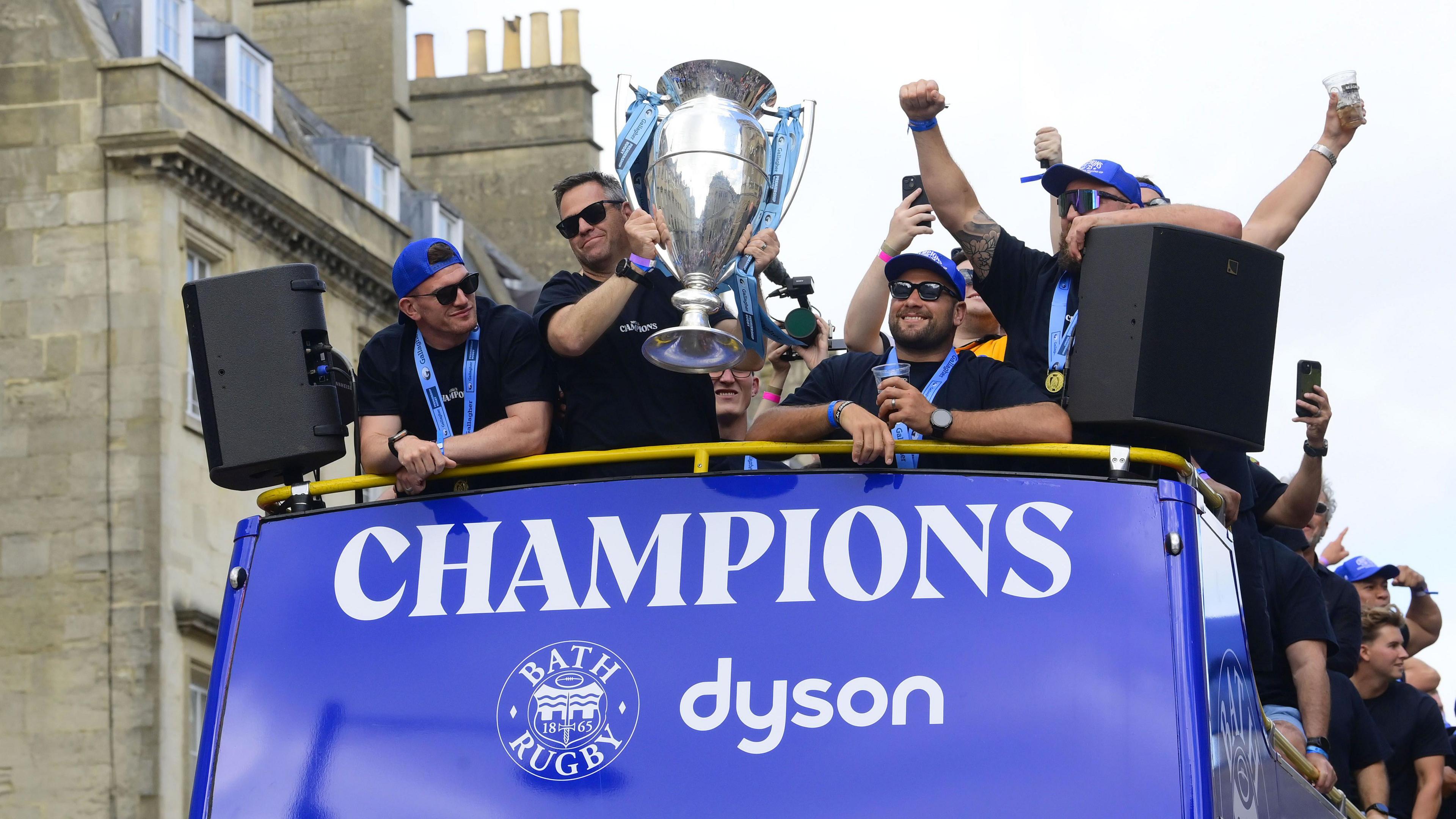 Bath head of rugby Johann van Graan (second left) holds the Prem Rugby trophy on the top of a bus with 'champions' written across the front
