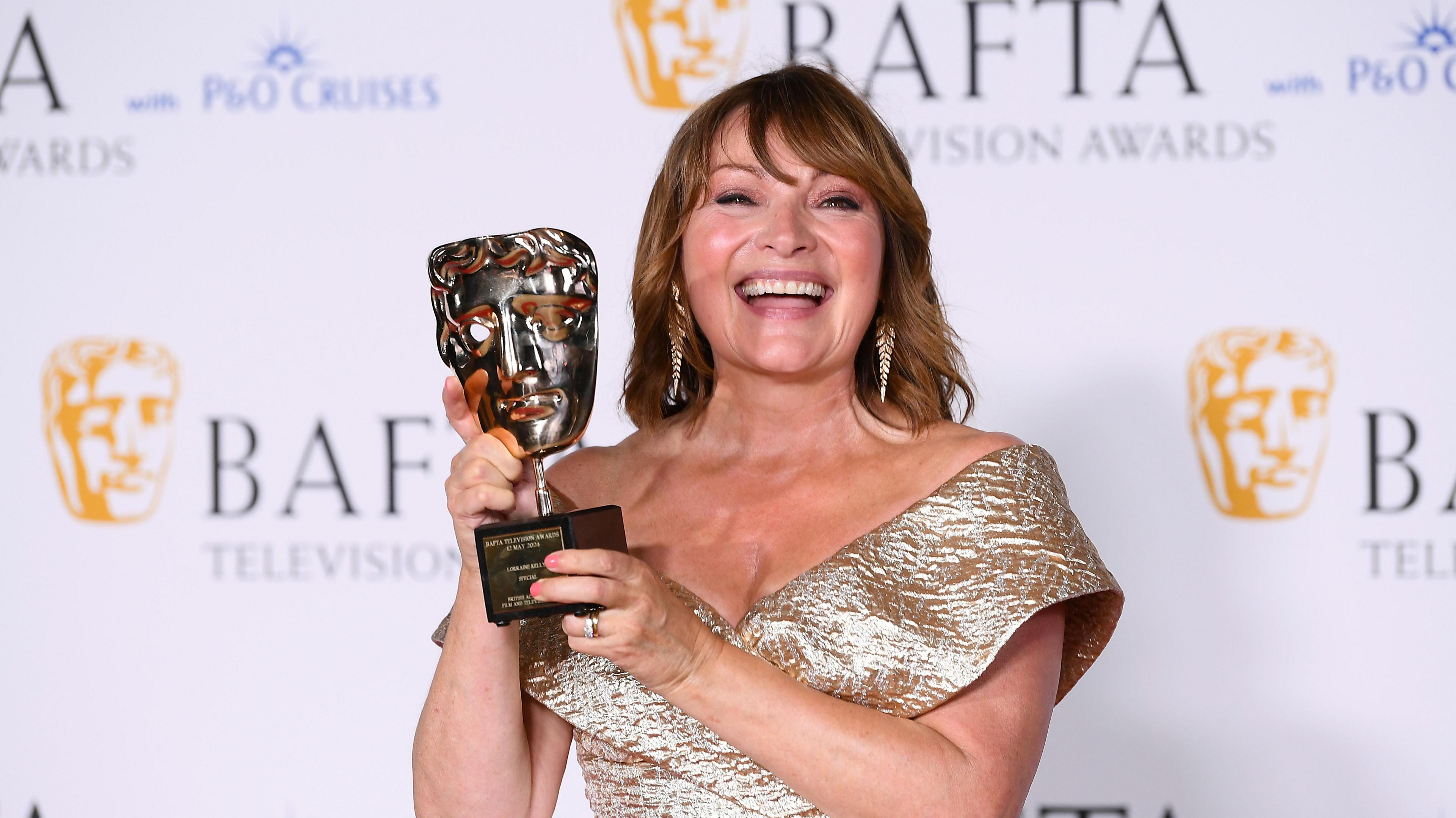 Lorraine Kelly smiling in a gold dress while holding a Bafta television award