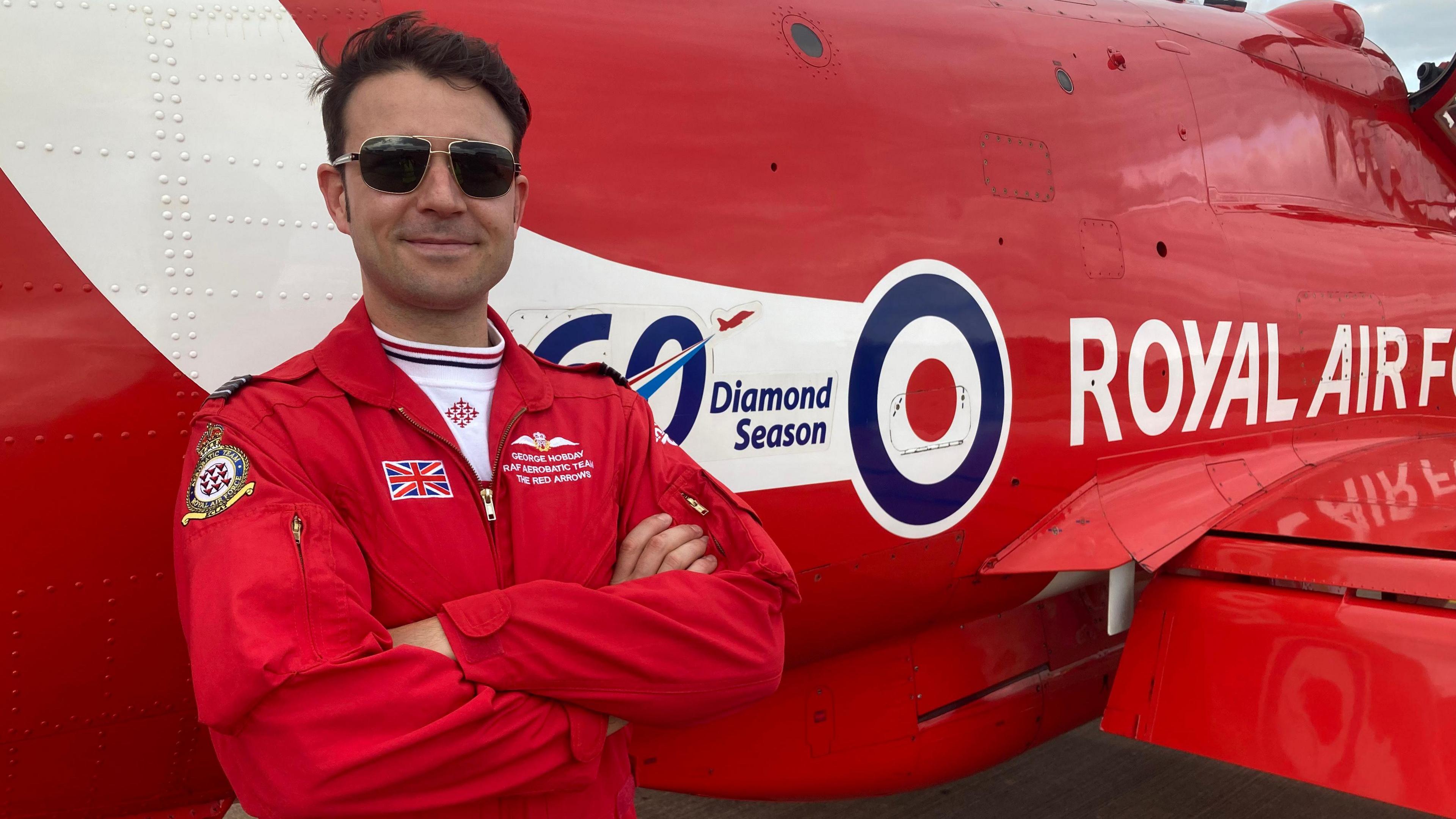 Red Arrows pilot George Hobday standing by his red arrow with his arms folded, smiling